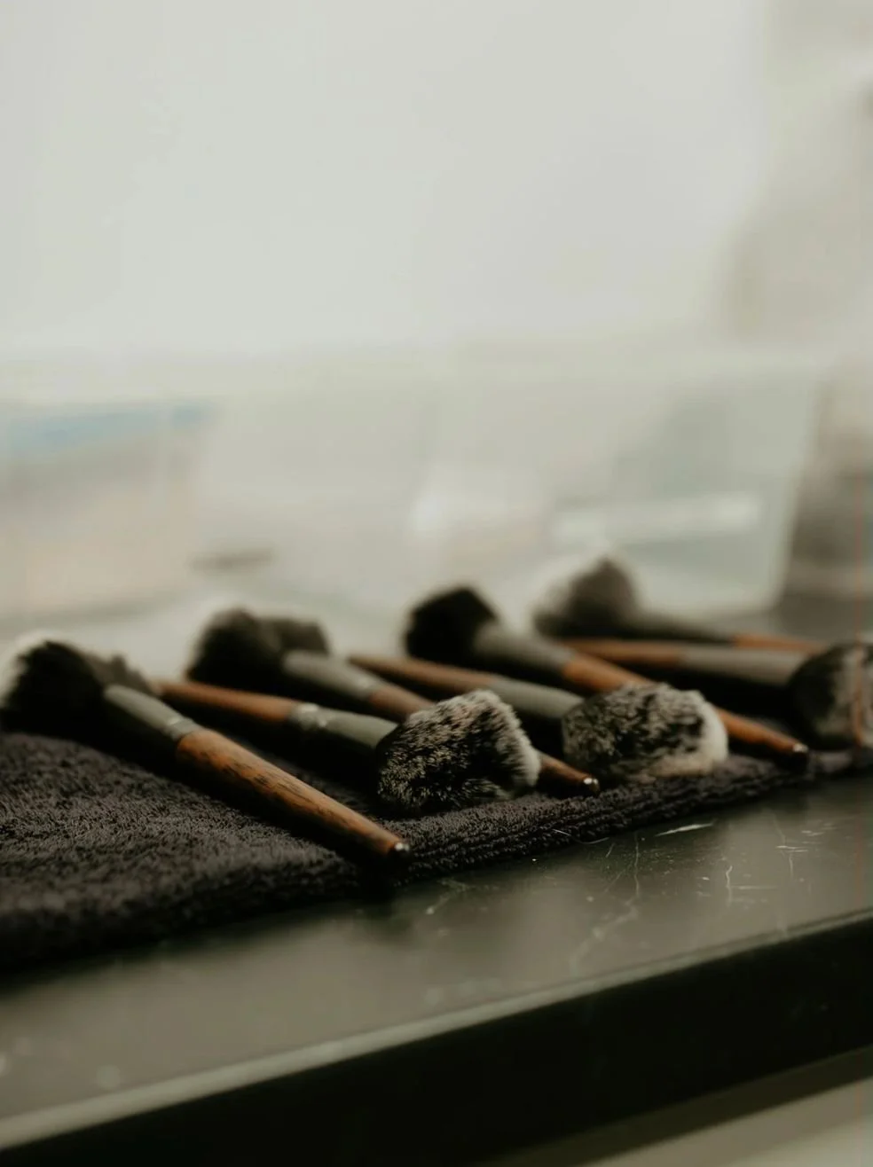 Makeup brushes with black bristles and wooden handles resting on a black towel.