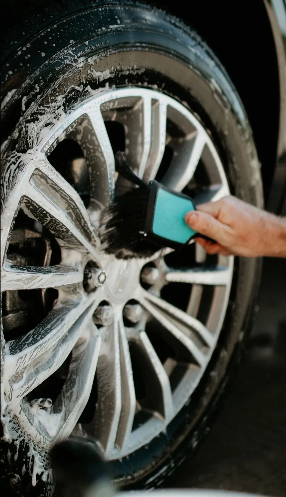 A person hand scrubbing a car wheel with soap and a brush during washing.