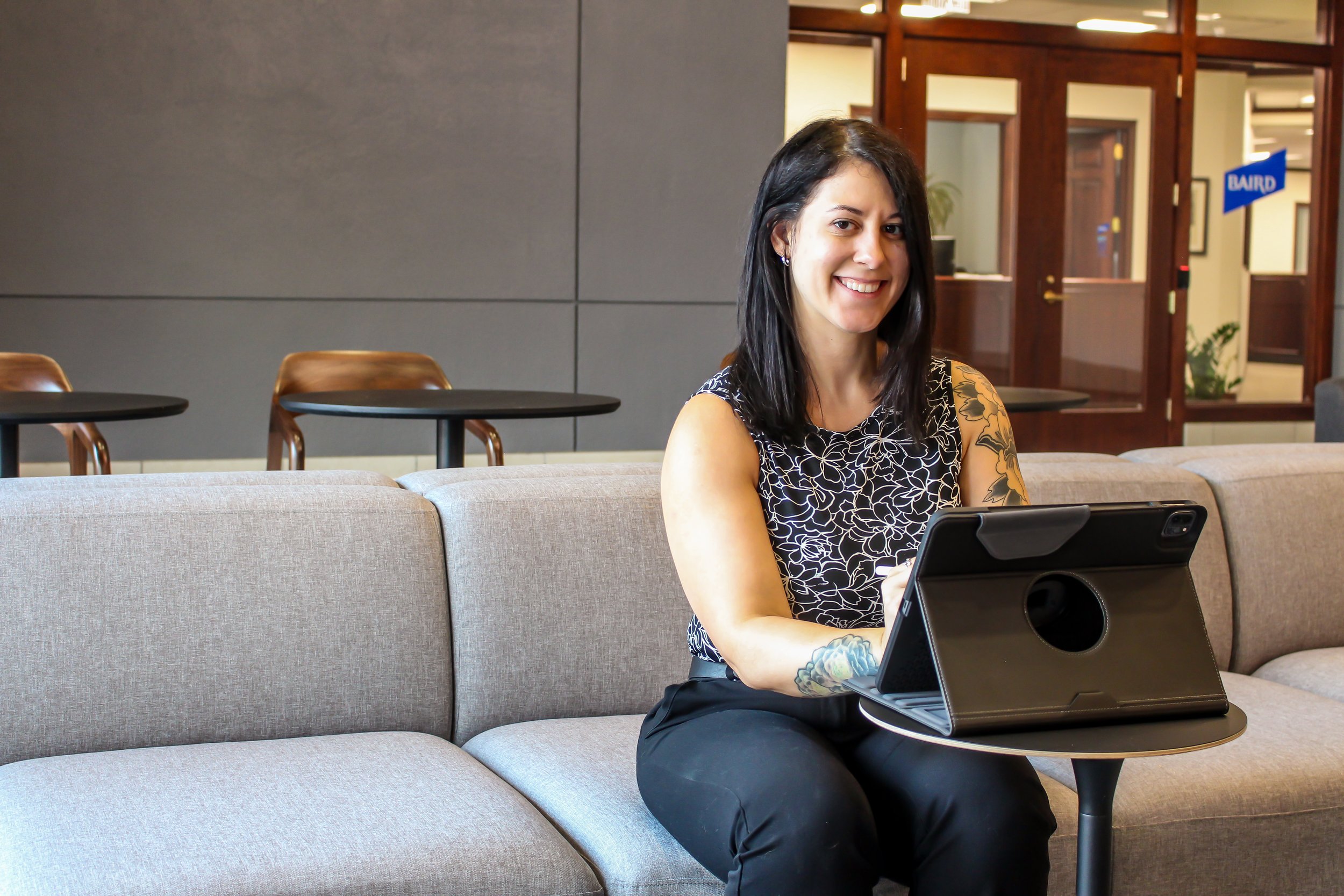 Smiling woman with tattoos using a tablet while seated on a lounge sofa
