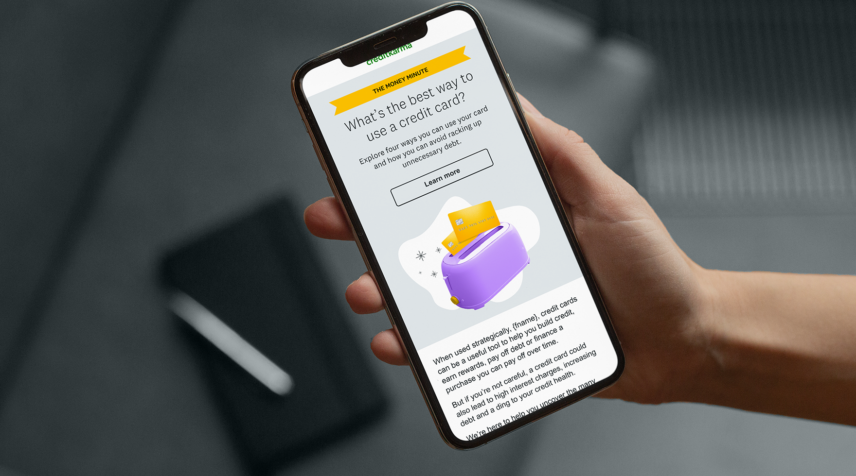 A person holding a smartphone displaying a webpage about using credit cards and financial tips, with a purple toaster illustration to the right of the text.