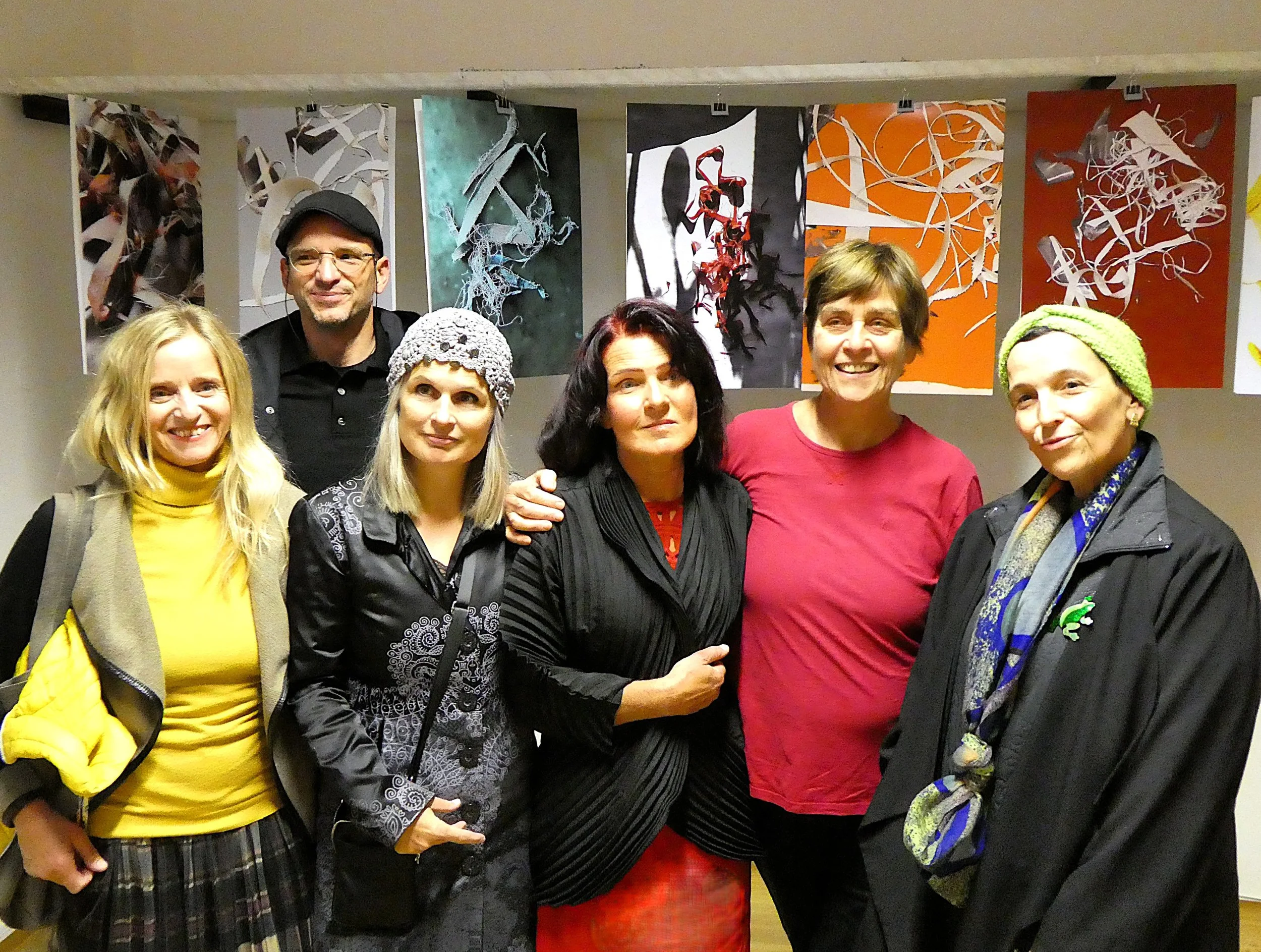 Gruppenfoto von sieben Menschen vor bunten abstrakten Gemälden in einem Ausstellungsraum.