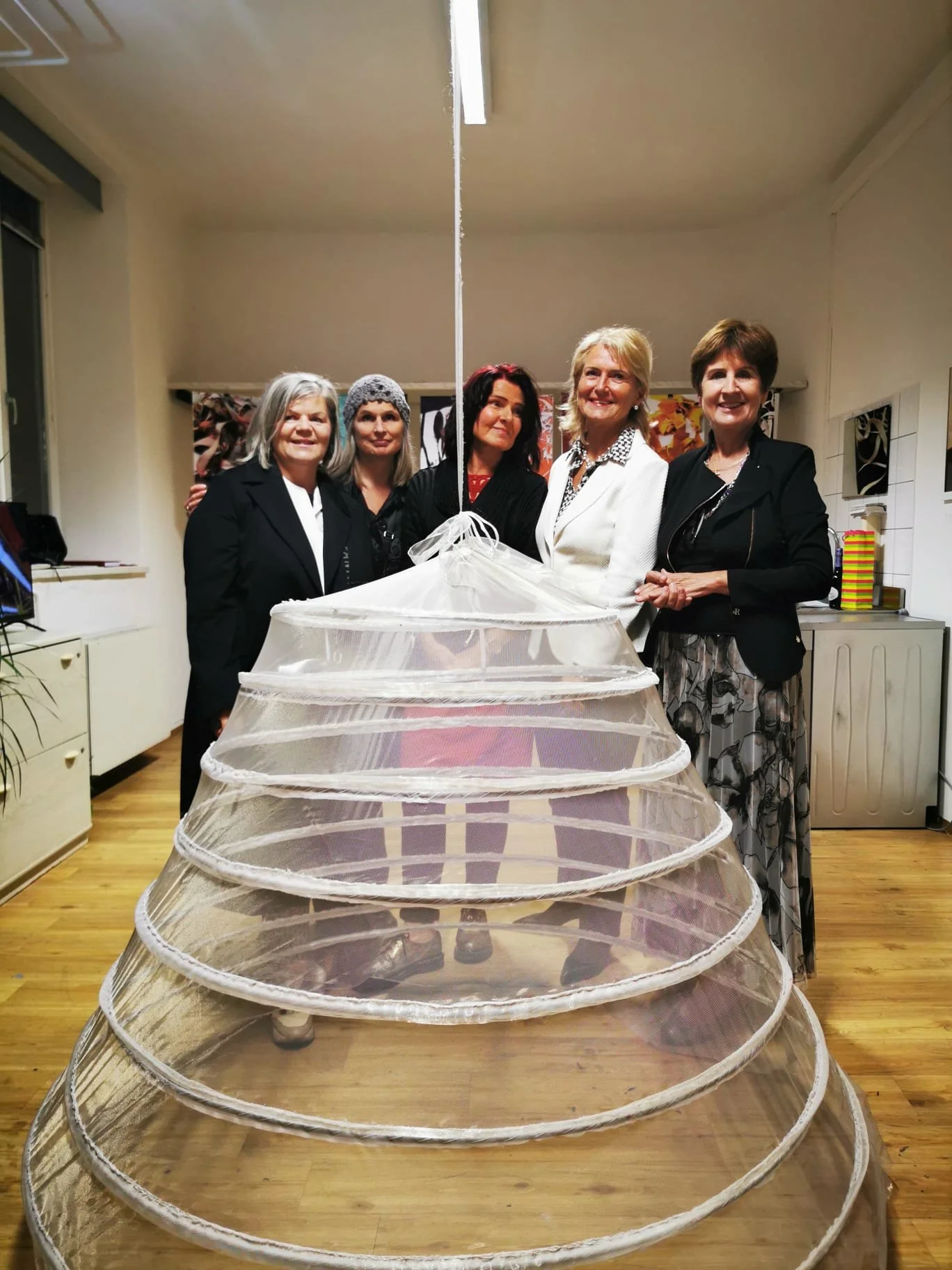 Fünf Frauen stehen hinter einem Reifrock-Exponat in einer Galerie und posieren für ein Foto.