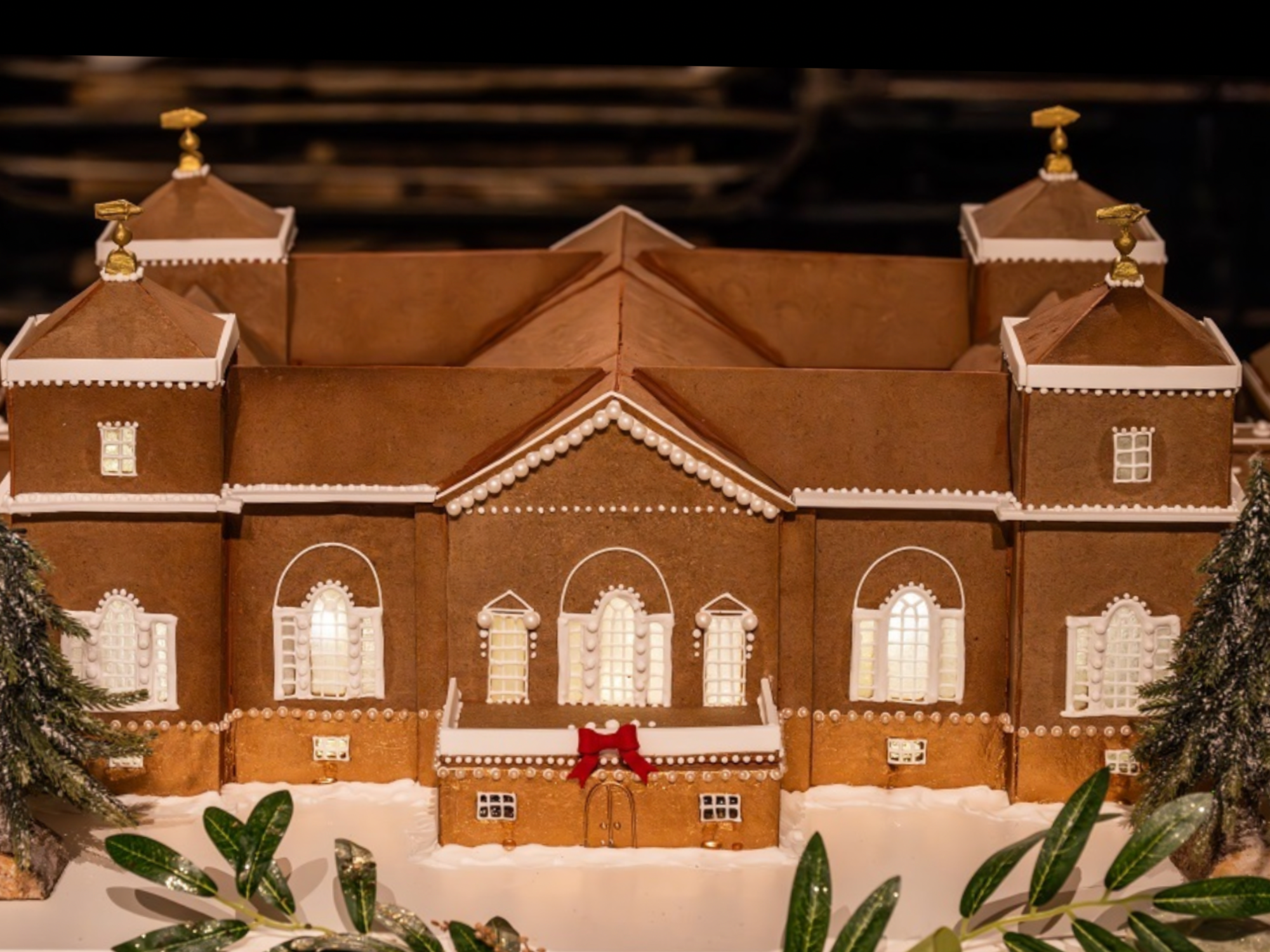 Gingerbread replica of Holkham Hall decorated with white icing, a red bow, and miniature trees, decorated for Christmas.