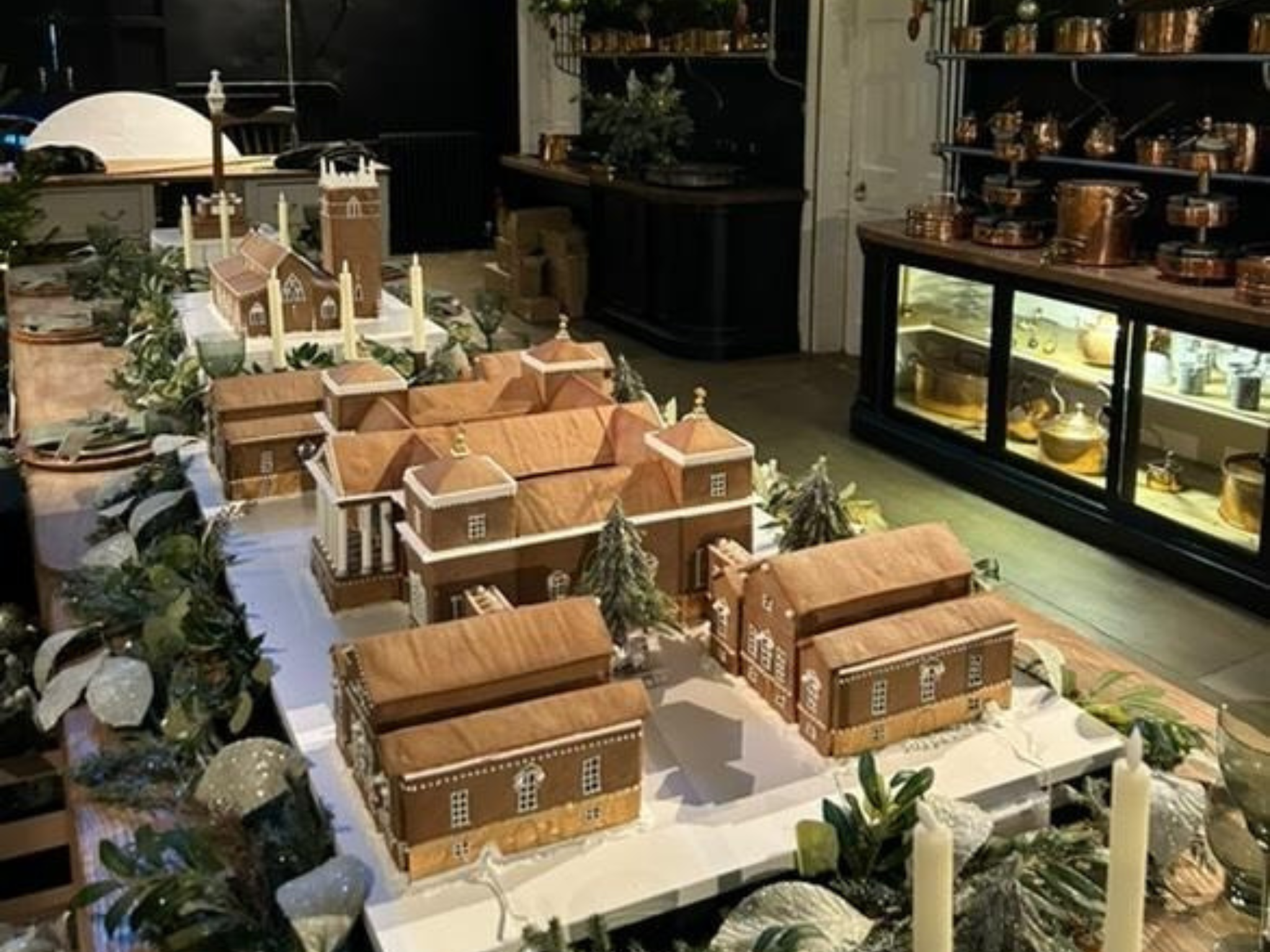 Decorative gingerbread house display of Holkham Hall with gingerbread replicas of each of the estate's buildings, surrounded by greenery and candles, displayed along the long table in the old kitchen of the hall.
