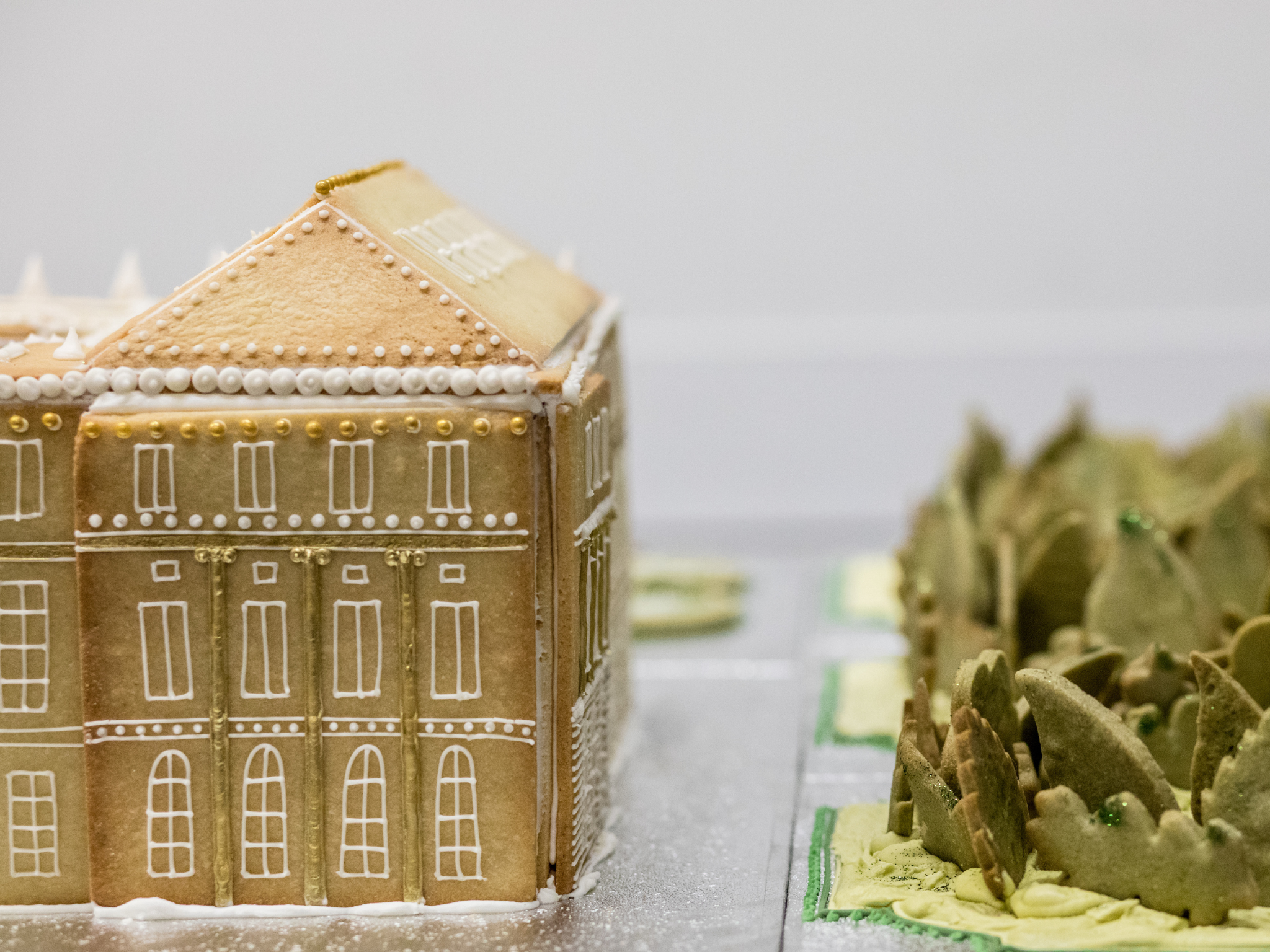 Decorated vanilla biscuit Palace of Versailles with intricate white icing details, set on a surface alongside matcha green tea biscuit ornamental gardens.