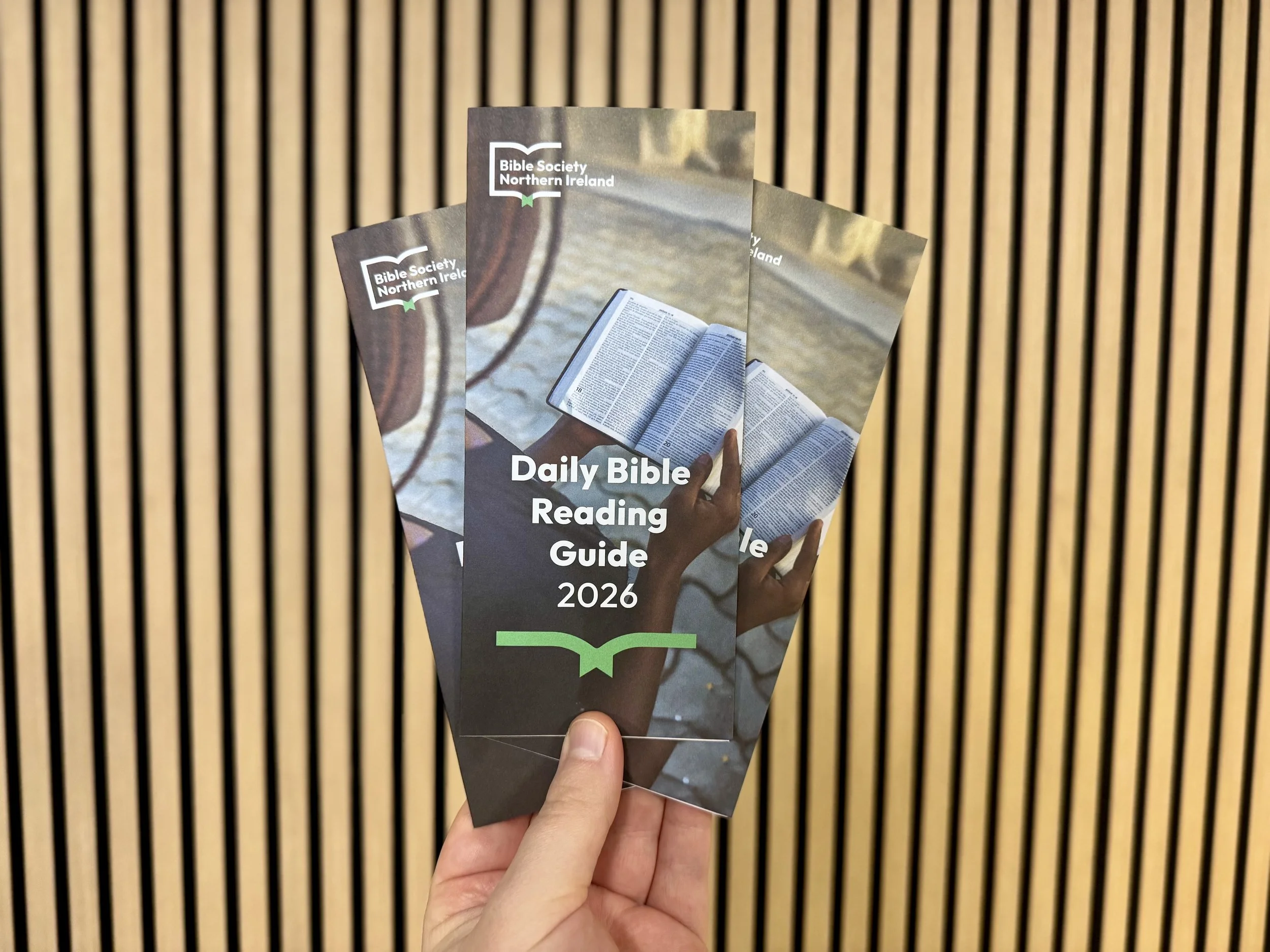 A person holds three copies of a "Daily Bible Reading Guide" brochure. The guides are titled Daily Bible Reading Guide and dated for 2026.