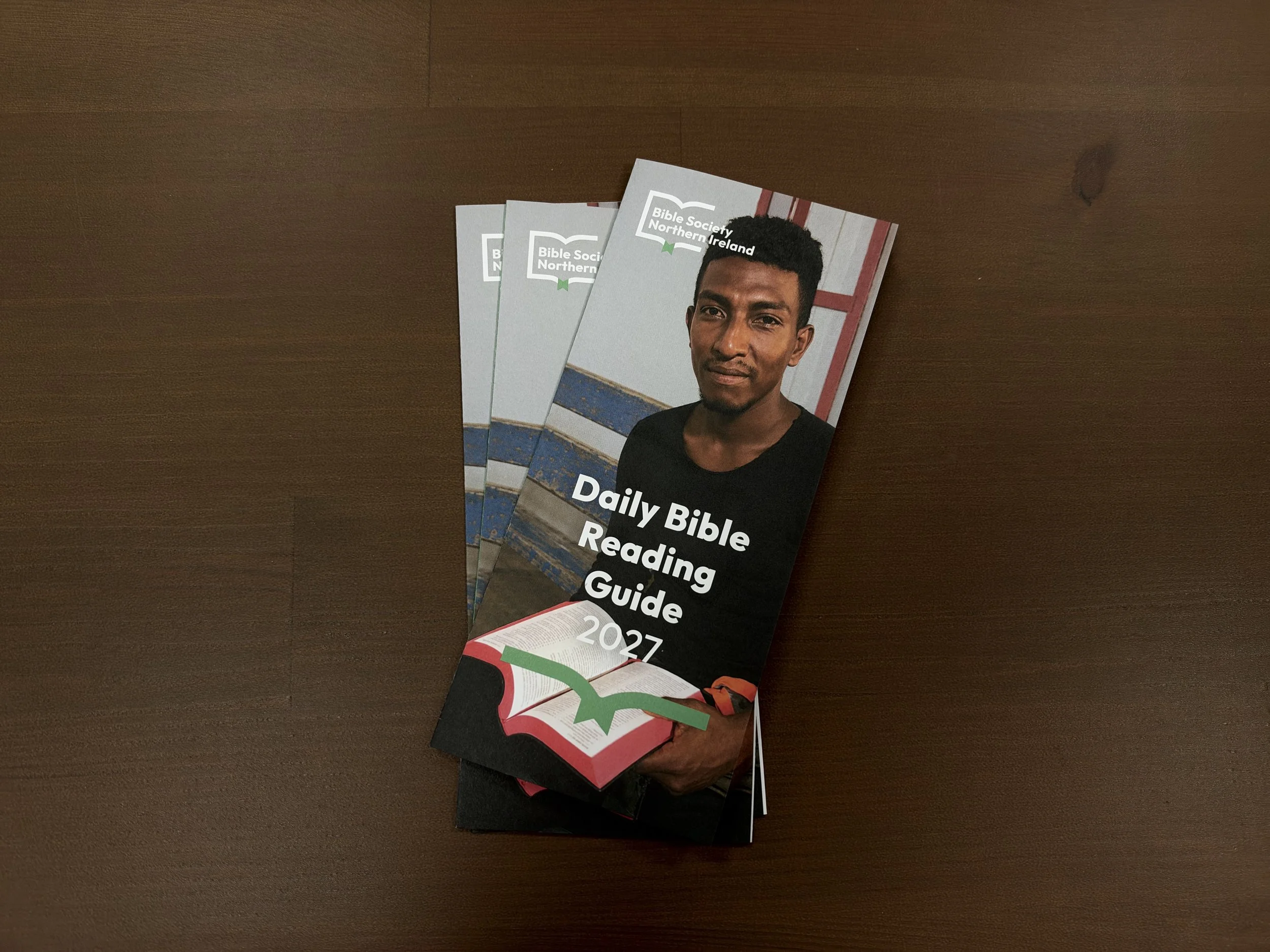A person holds three copies of a "Daily Bible Reading Guide" brochure. The guides are titled Daily Bible Reading Guide and dated for 2026.