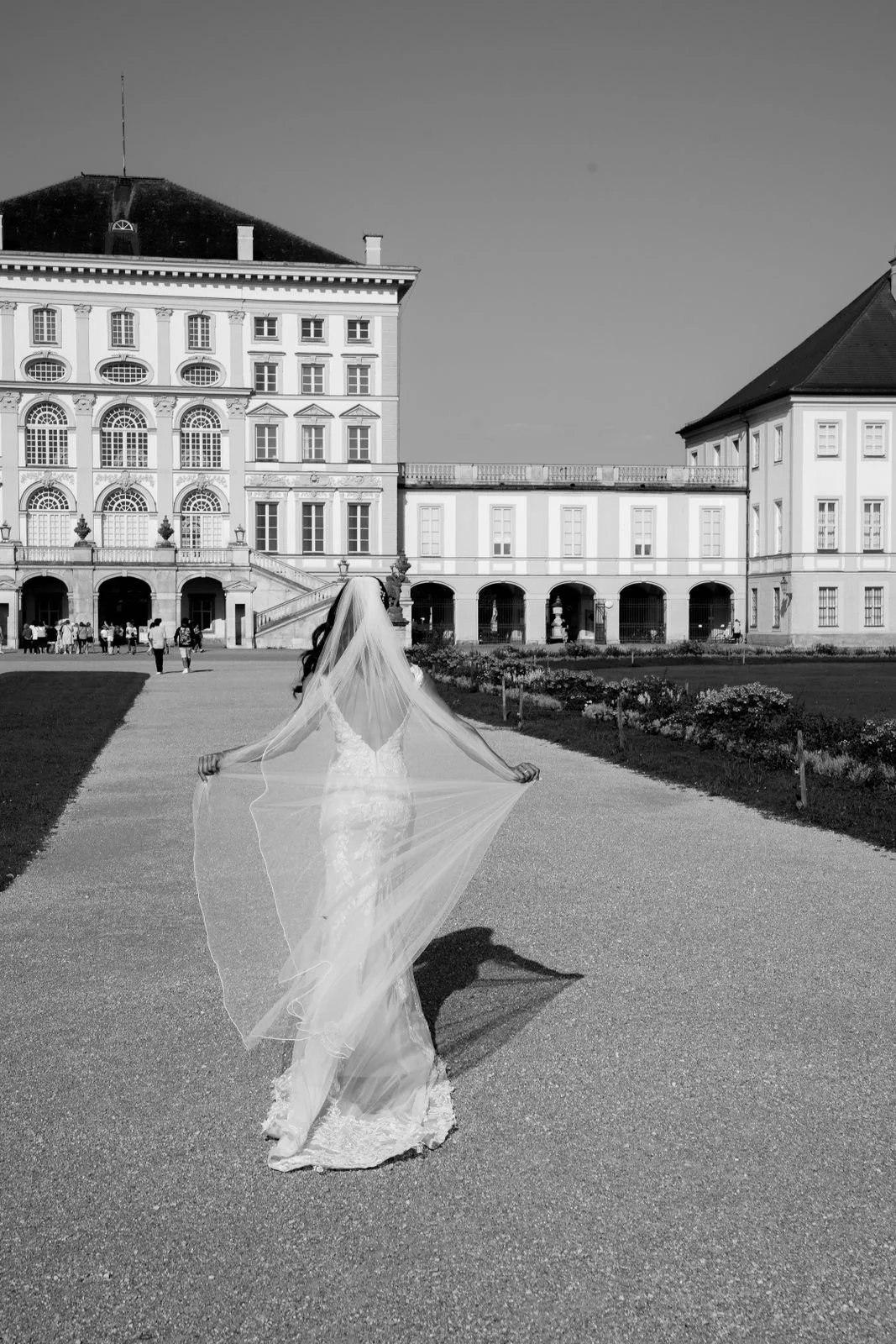 Braut in Hochzeitskleid mit Schleier von hinten vor einem historischen Gebäude, schwarz-weiß Foto.