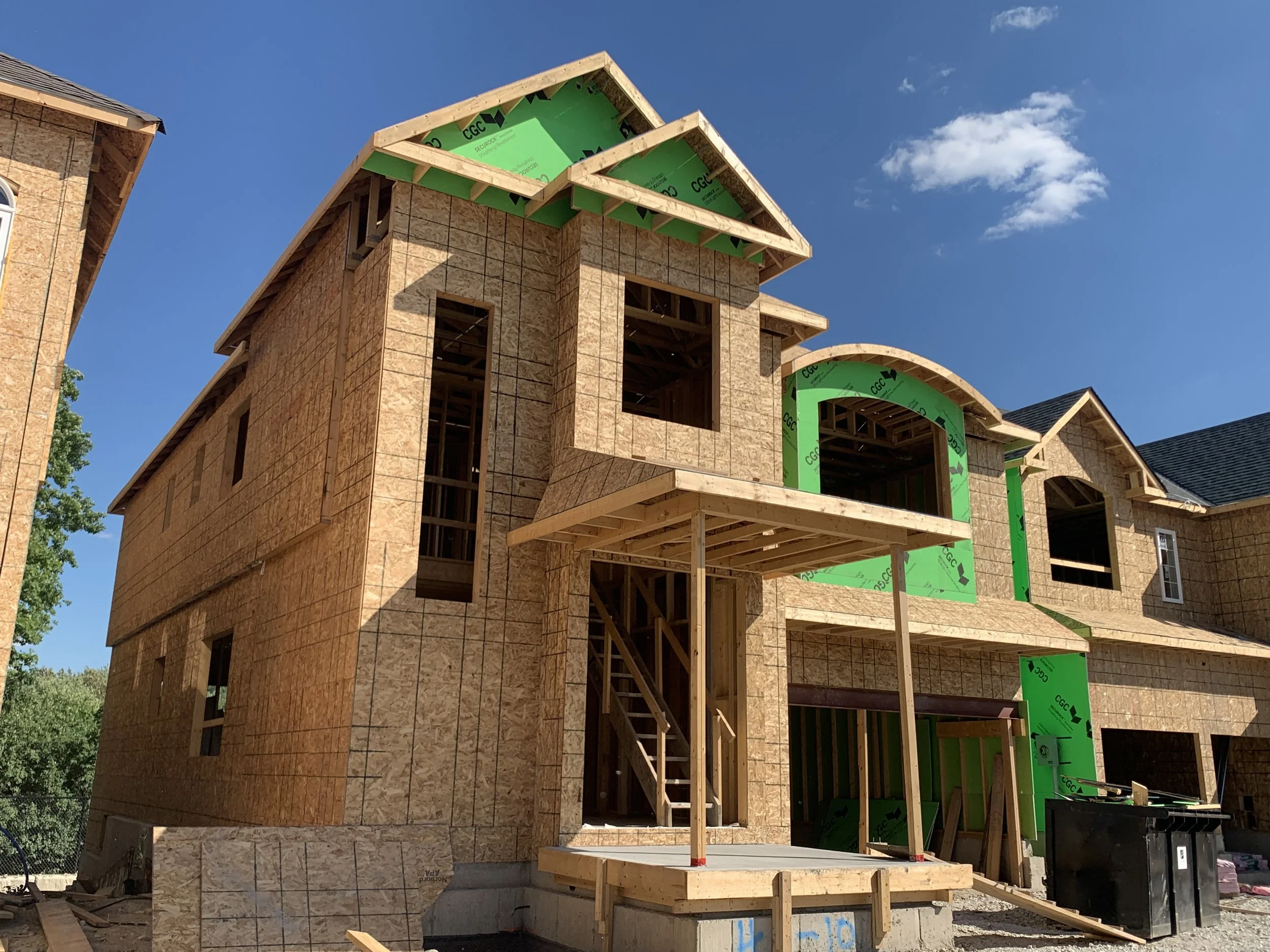 New house under construction with exposed wood framing and green insulation panels.