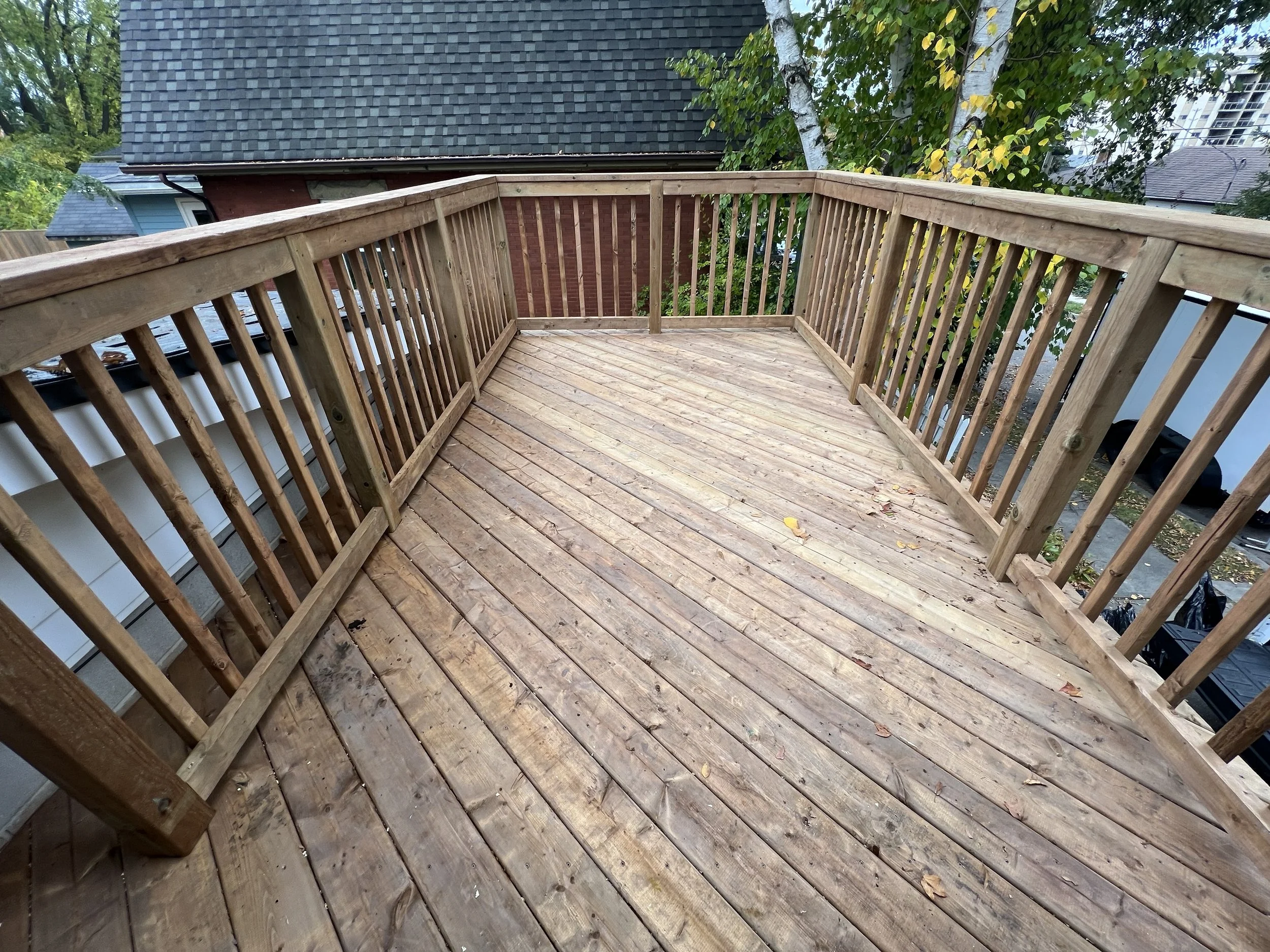 Wooden deck with railing, surrounded by trees and rooftops.