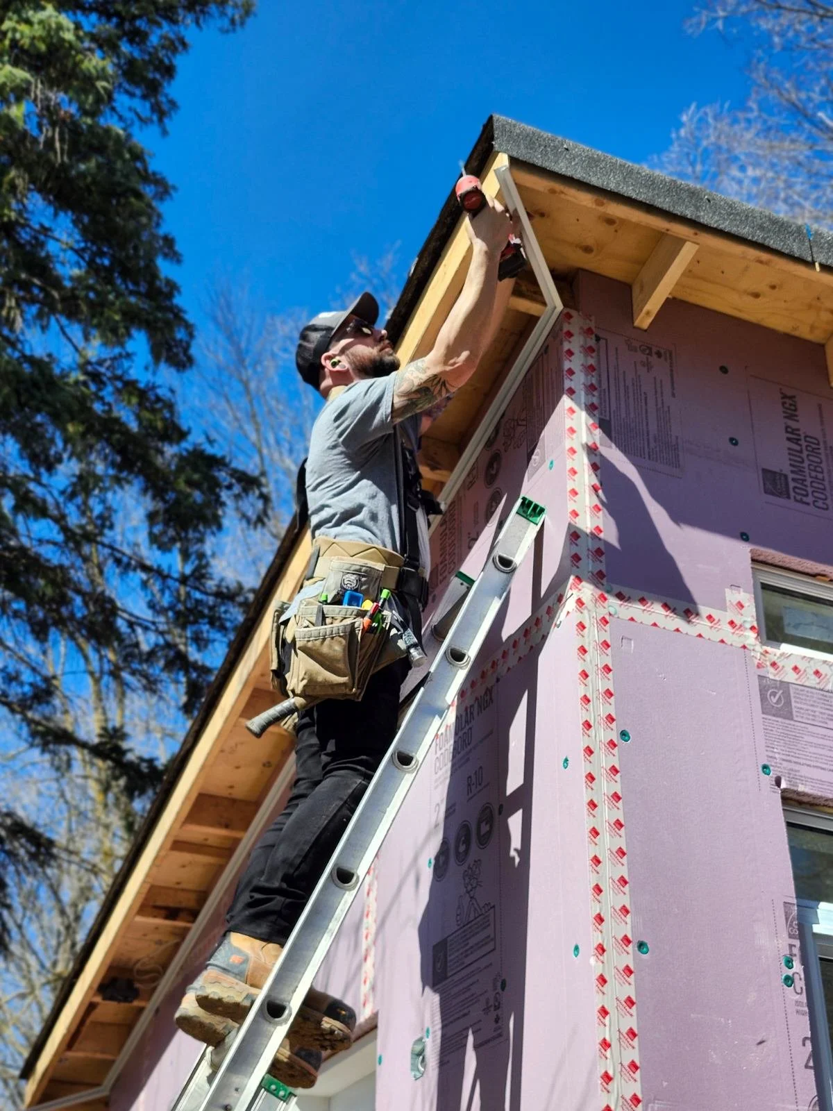 Construction worker on a ladder working on the roof of a house under a clear blue sky