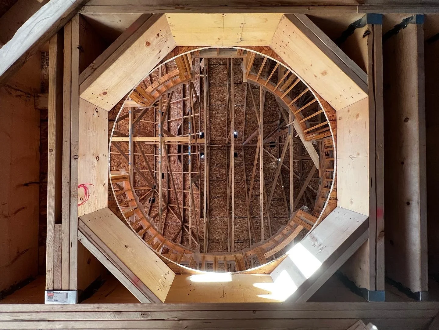 Interior view of a wooden dome structure under construction, featuring exposed beams and plywood framework forming a circular shape.