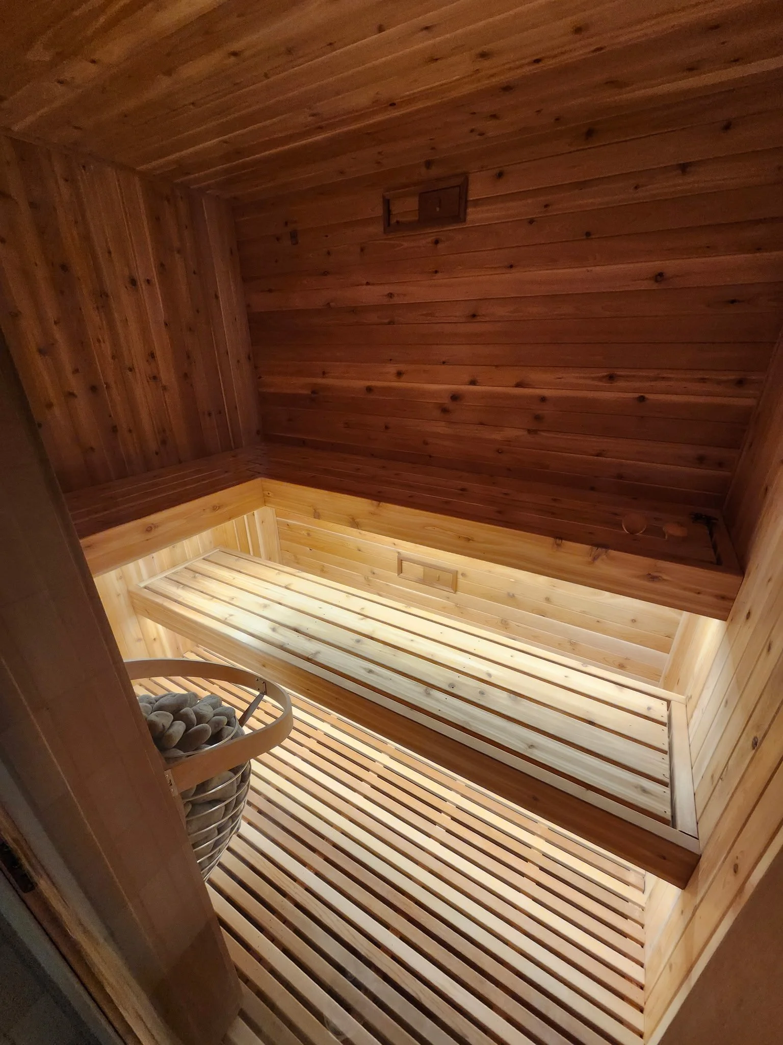 Interior view of a wooden sauna with a slatted bench, a HUUM stone sauna heater, and wooden walls and ceiling.