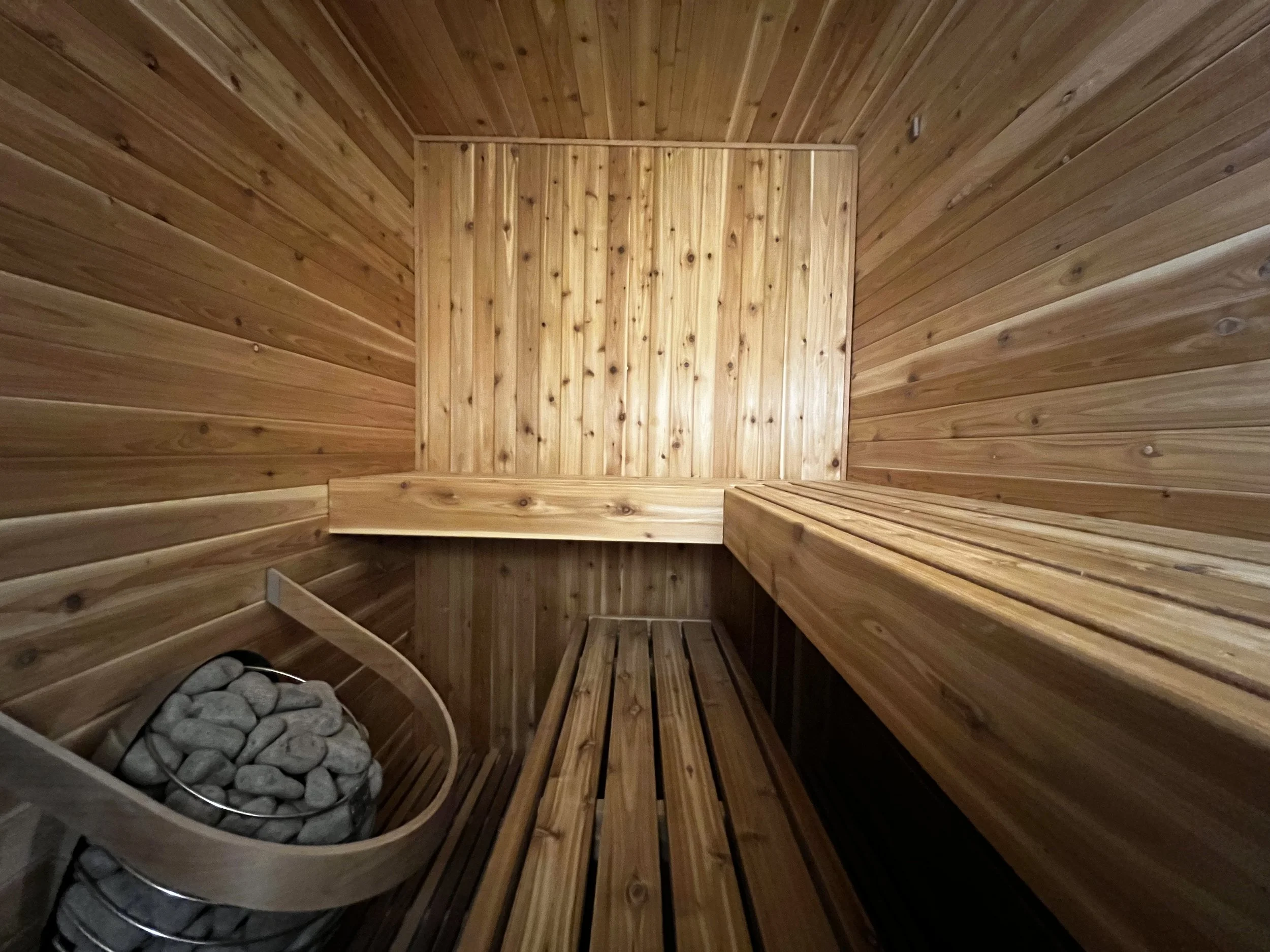 Interior view of a wooden sauna with benches and a heater filled with stones.