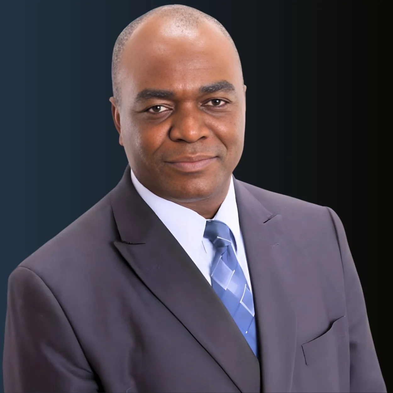 Professional headshot of a man in a suit and tie, with a dark background.