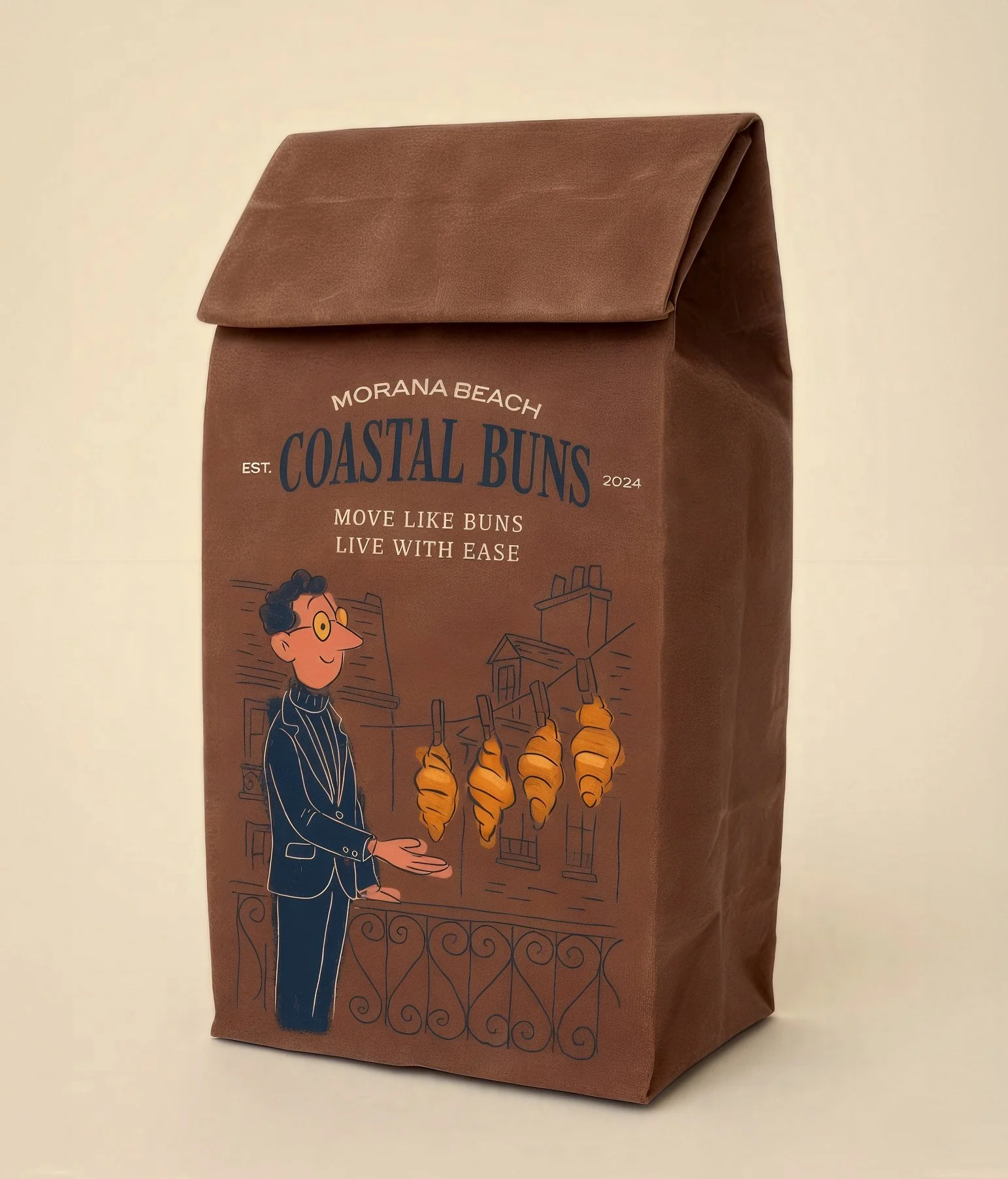 A brown paper bag with a printed design featuring a man in a suit holding a tray of croissants, with text that reads 'Morana Beach Coastal Buns, Est. 2024, Move Like Buns Live with Ease' and an illustration of a seaside town.