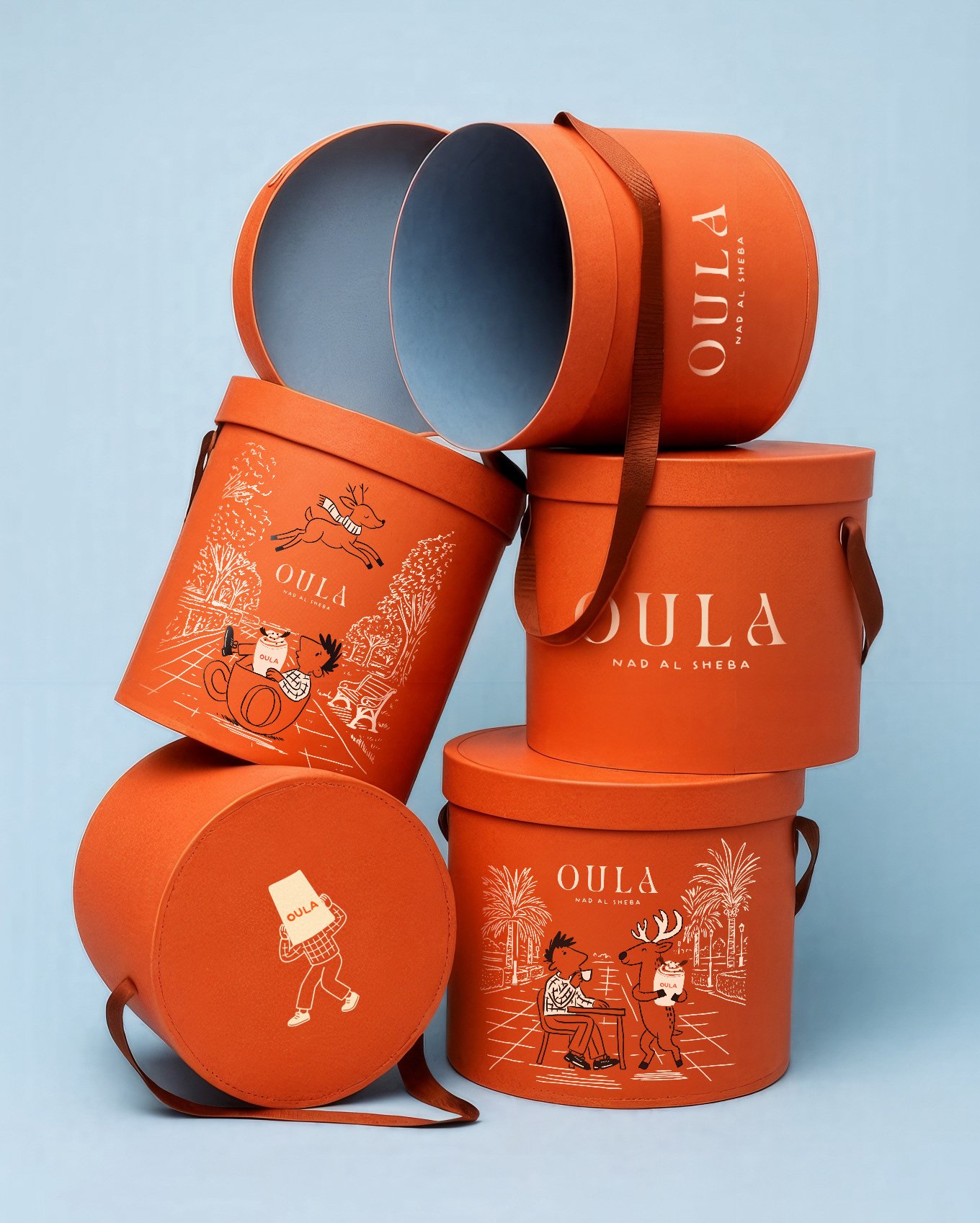Stacked orange travel and storage containers with the brand name "OULA" and cartoon illustrations of animals and trees, against a light blue background.
