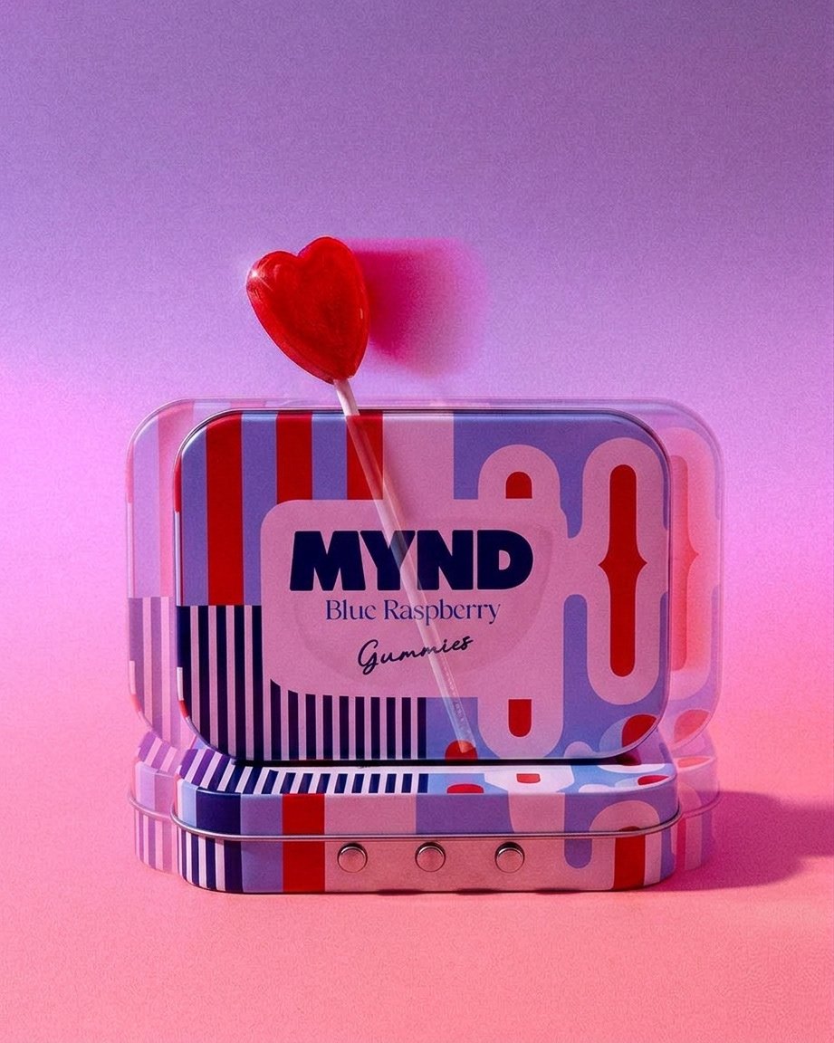 A decorative tin container of MYND Blue Raspberry Gummies with a red heart-shaped lollipop on top, against a pink background.