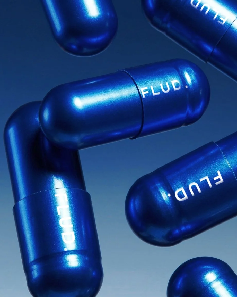Several blue capsules with the word "FLUD!" written on them, floating against a dark background.