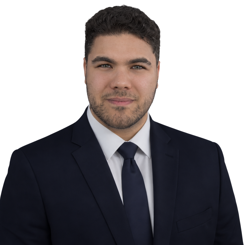 A young man wearing a black suit, white shirt, and black tie, looking confidently at the camera.
