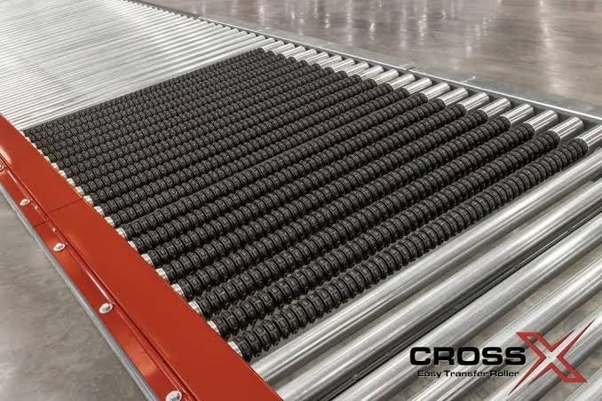 Roach Conveyors CrossX easy transfer roller installed on a conveyor with metal rods situated on a conveyor bed between a red frame.