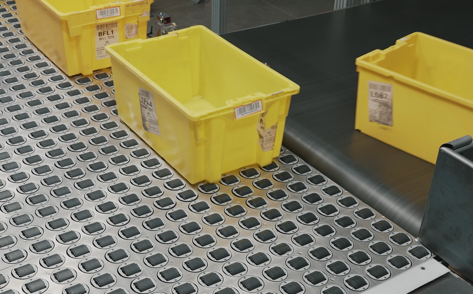 A steerable roller sorter table diverting yellow totes at 90 degrees onto a black conveyor belt.