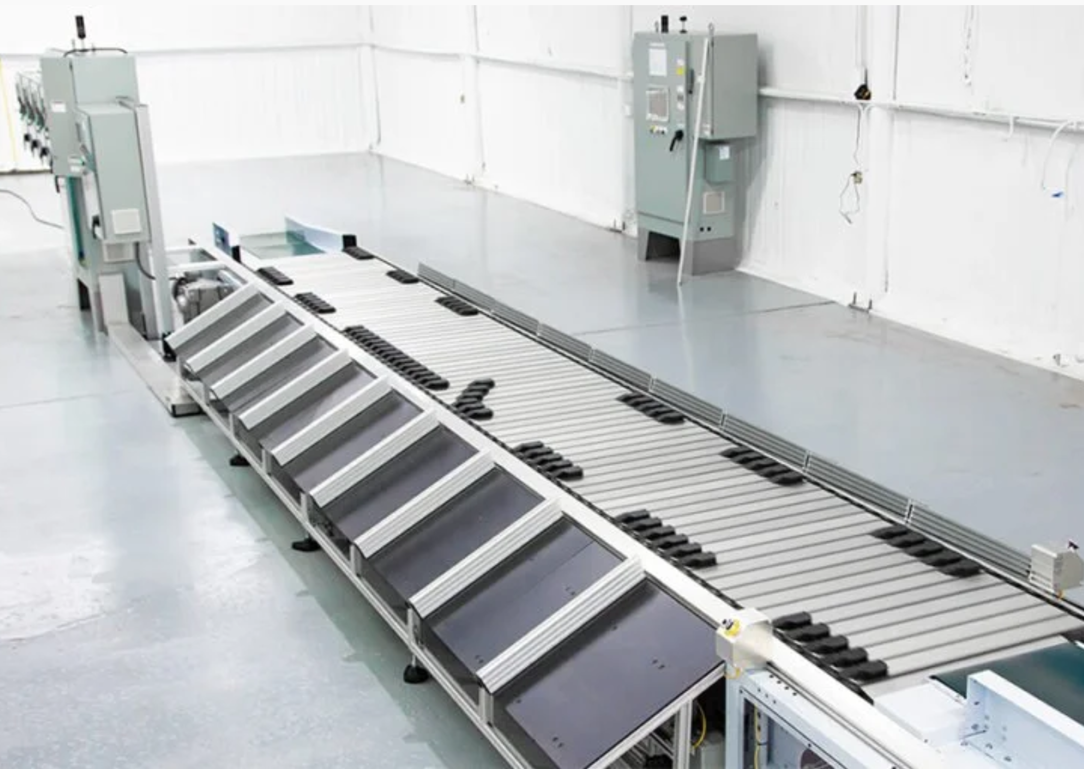 Large conveyor system with multiple sections and rollers, set up in a clean, industrial space with electrical panels on the walls.