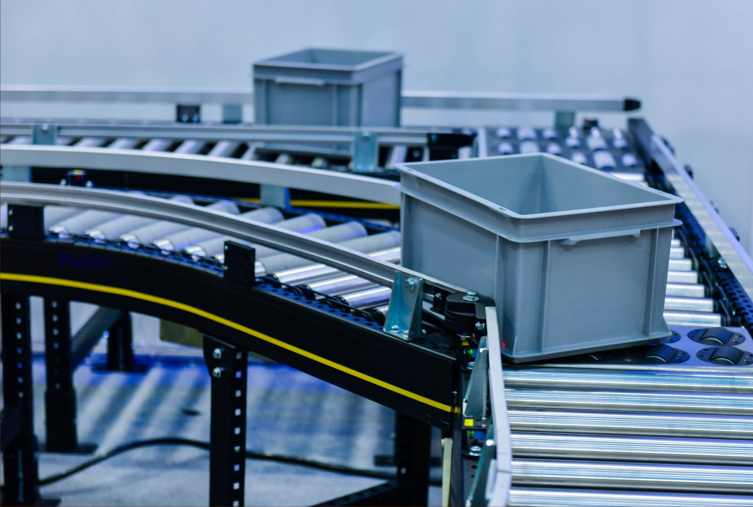 Tote being conveyed on MDR conveyor with silver colored rollers and dark exterior.