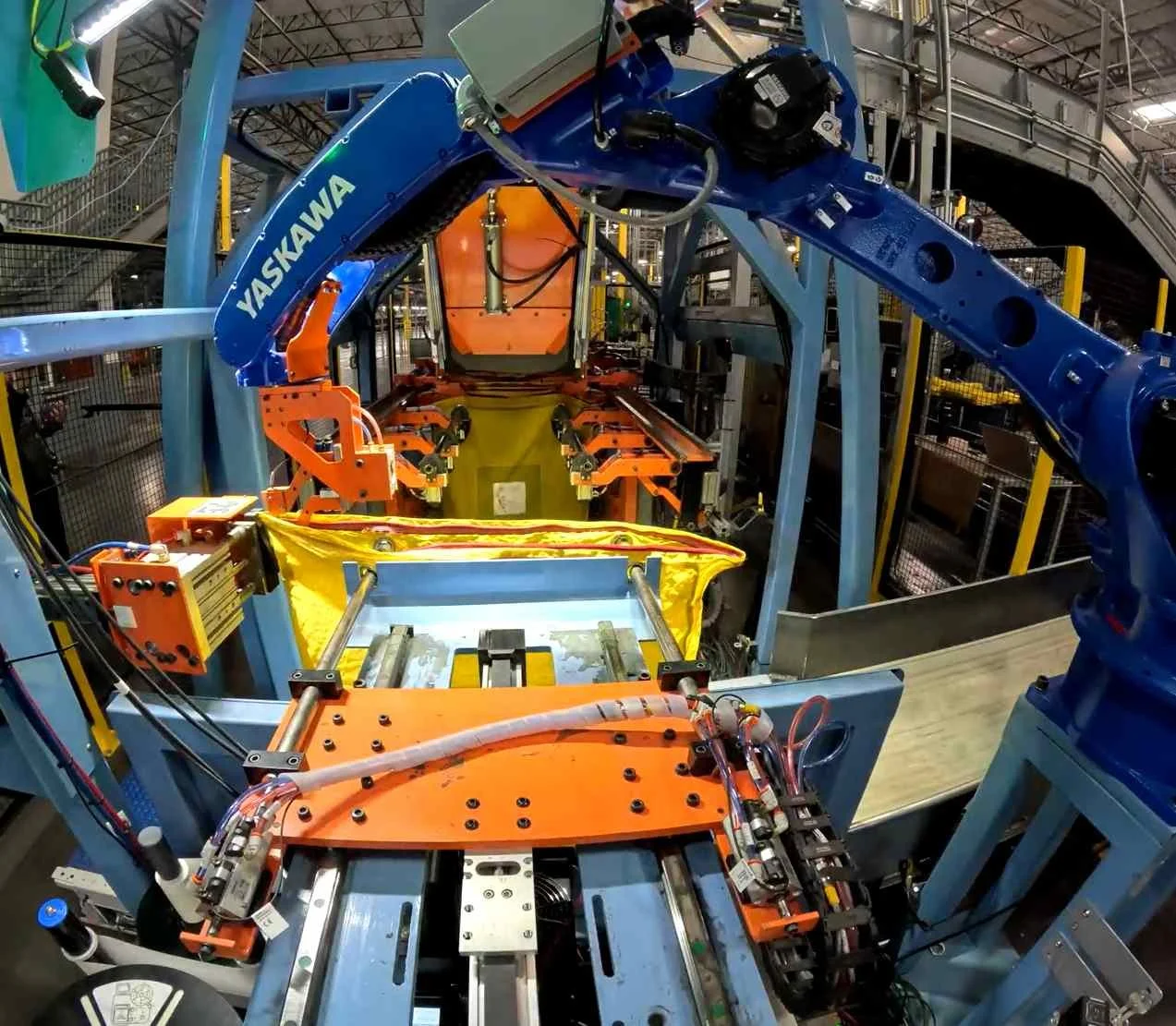 Blue robotic arm positioned to zip bag containing parcels in automated distribution facility.
