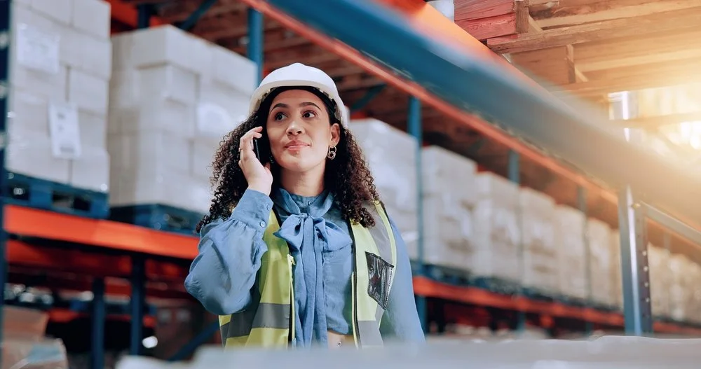 Woman talking on cell phone in front of distribution center racking about automating distribution operations and warehouses.