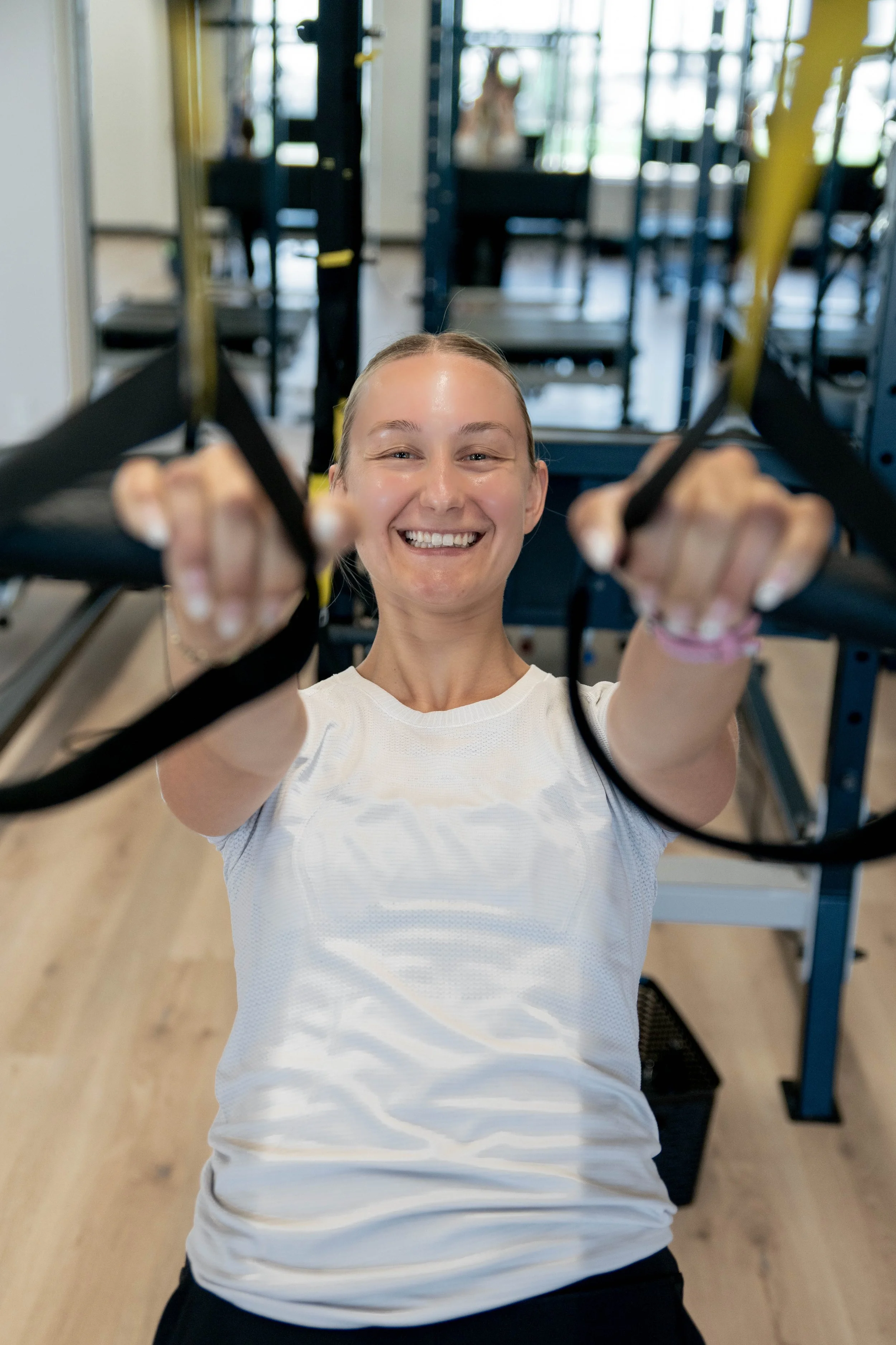 A young woman smiling and using resistance bands during a workout at the gym.