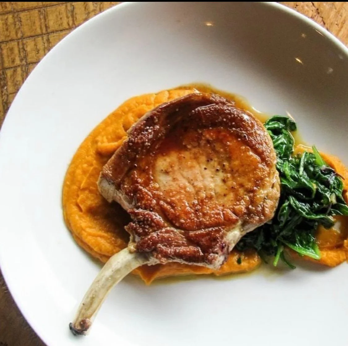 A plate with a cooked pork chop on a bed of sweet potato mash, topped with seasoned greens.