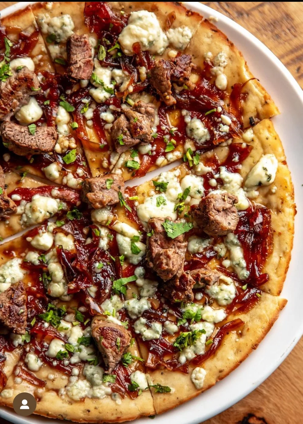 Close-up of a pizza with beef, caramelized onions, blue cheese, chopped parsley, and tomato sauce on a golden crust.