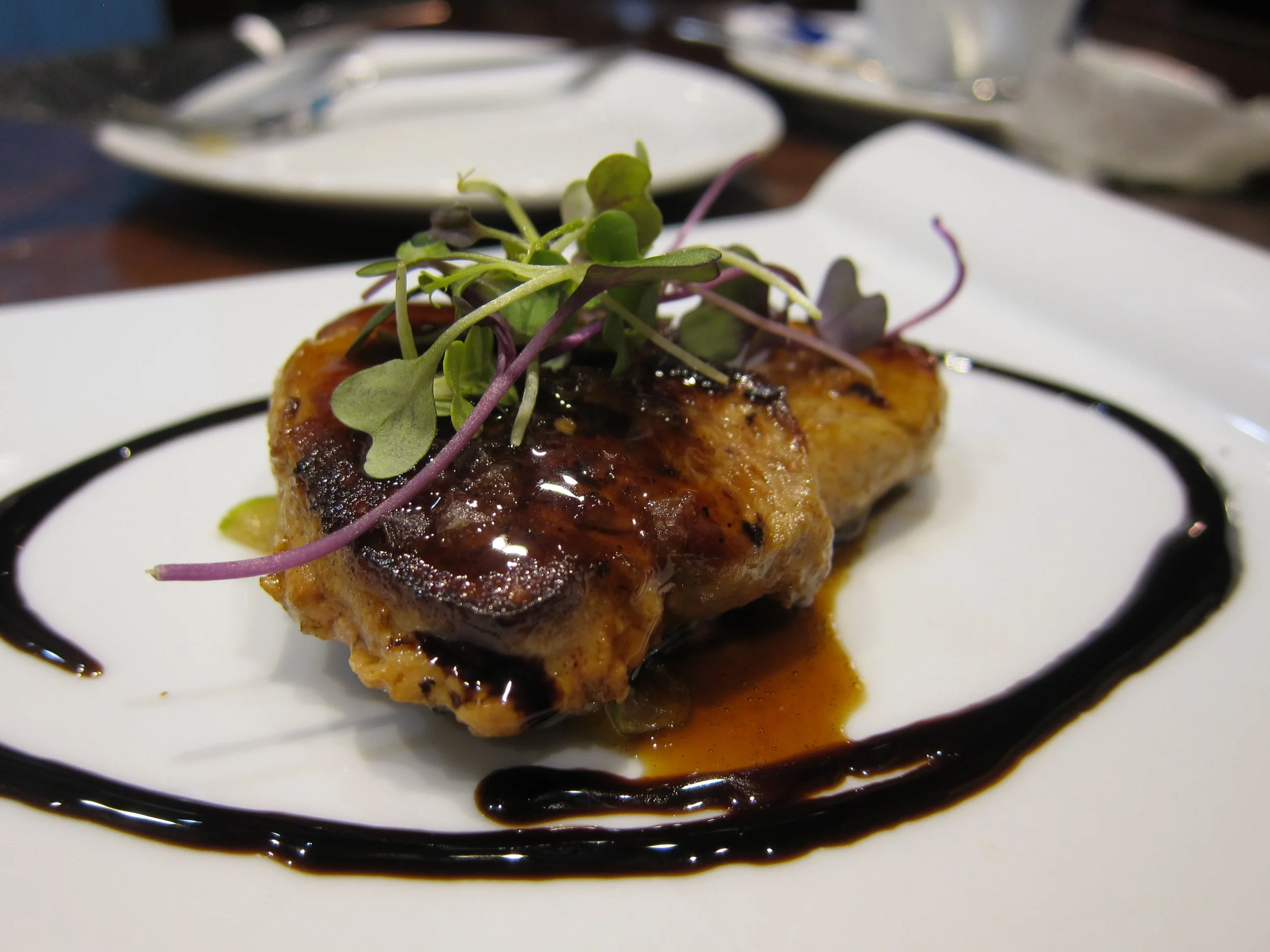 Grilled chicken breast topped with microgreens and sauce, served on a white plate with a decorative sauce swirl.