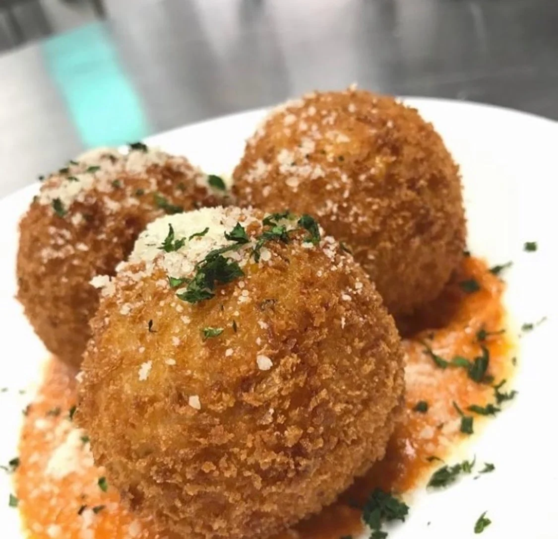 Three crispy fried arancini balls garnished with chopped herbs, served on a plate with tomato sauce.