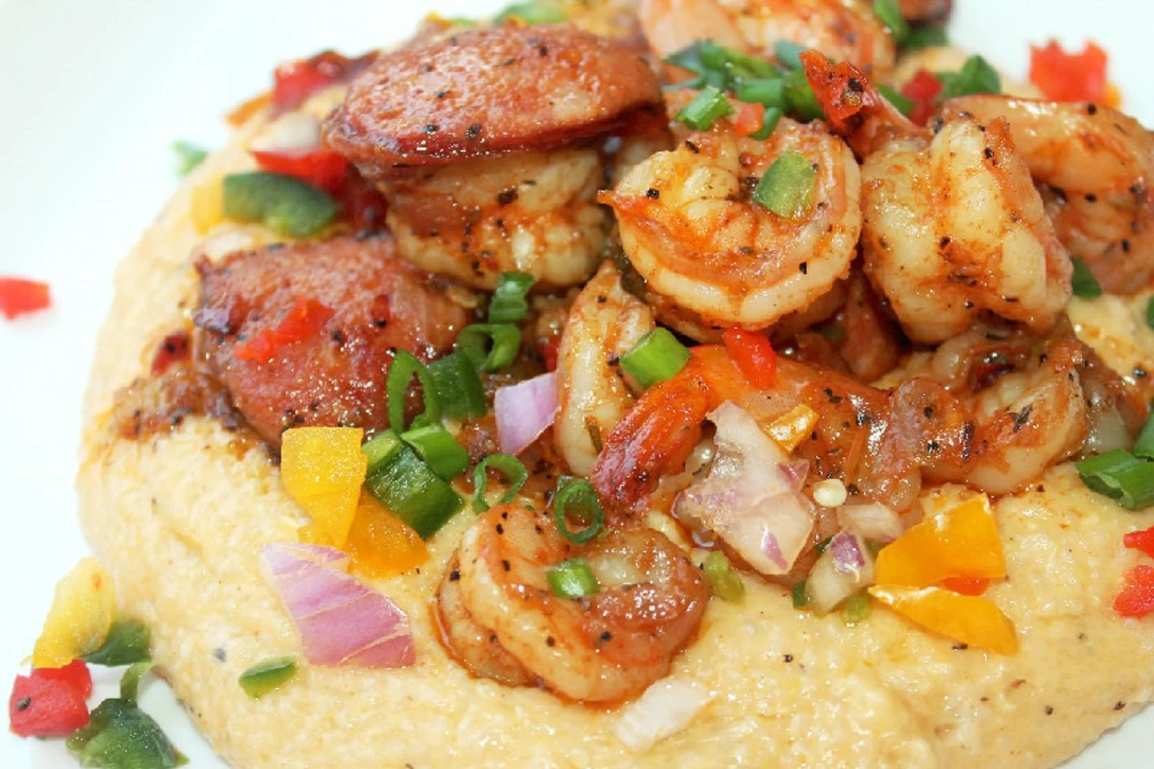 Shrimp and sausage topped with chopped green, red, yellow, and purple onions and peppers on a bed of polenta