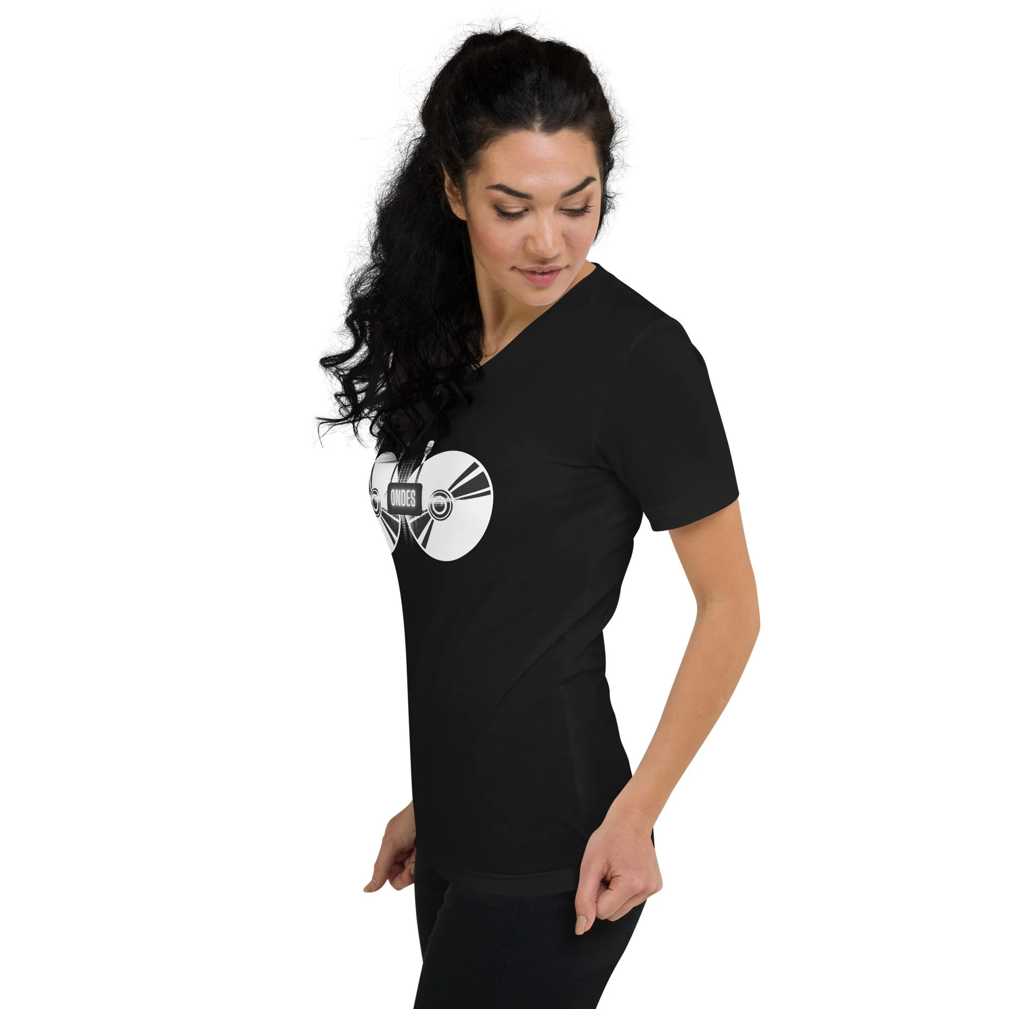 Woman with dark curly hair wearing a black T-shirt with a graphic of a CD and the word 'ONES'. She is looking down and slightly to the side, standing against a white background.