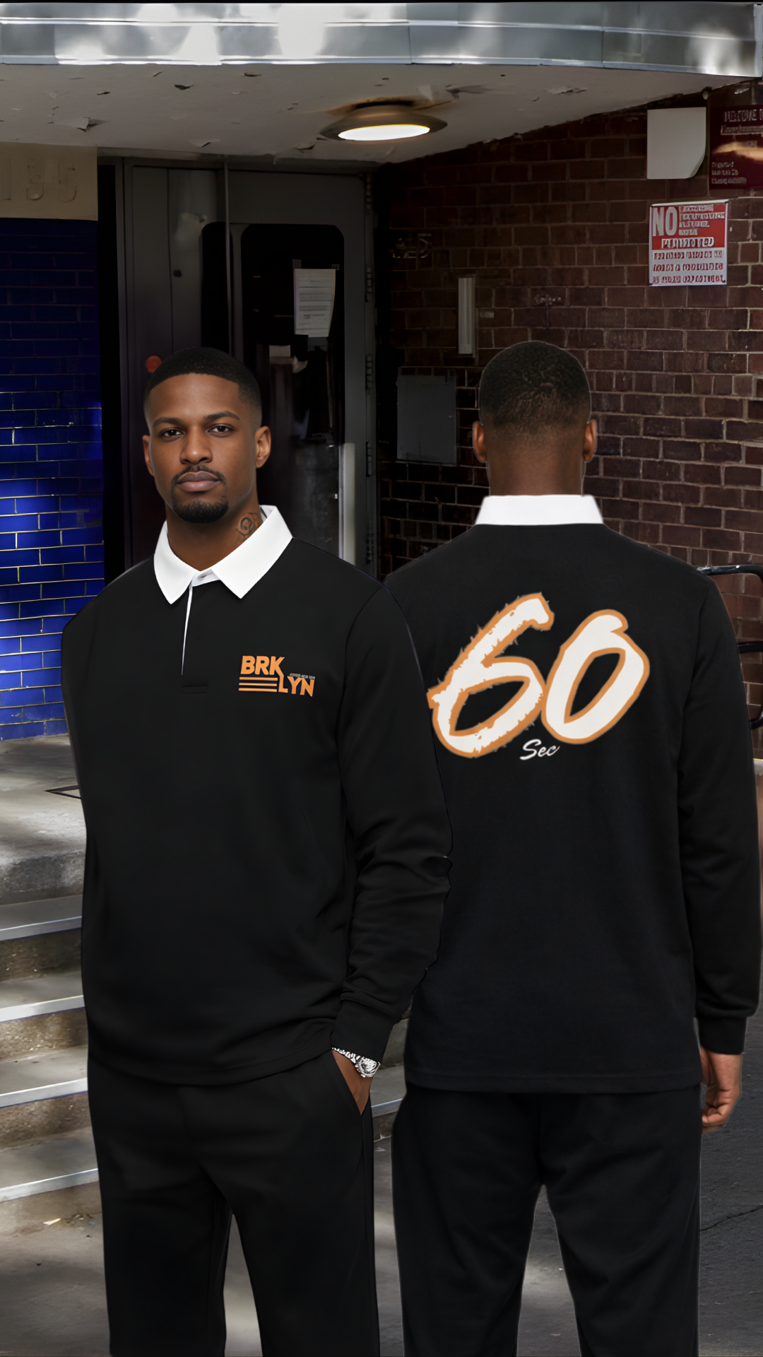 Two men standing outdoors in front of a brick building, wearing black jackets with orange and white text, one facing forward and the other with his back to the camera.