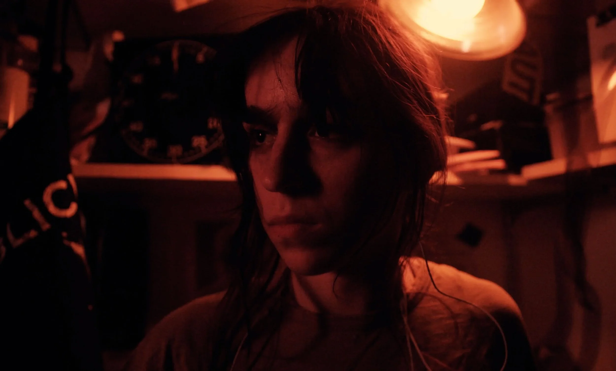 A woman with wet hair leaning forward, illuminated by warm red and orange lighting in a dark room, with a background of shelves and boxes.