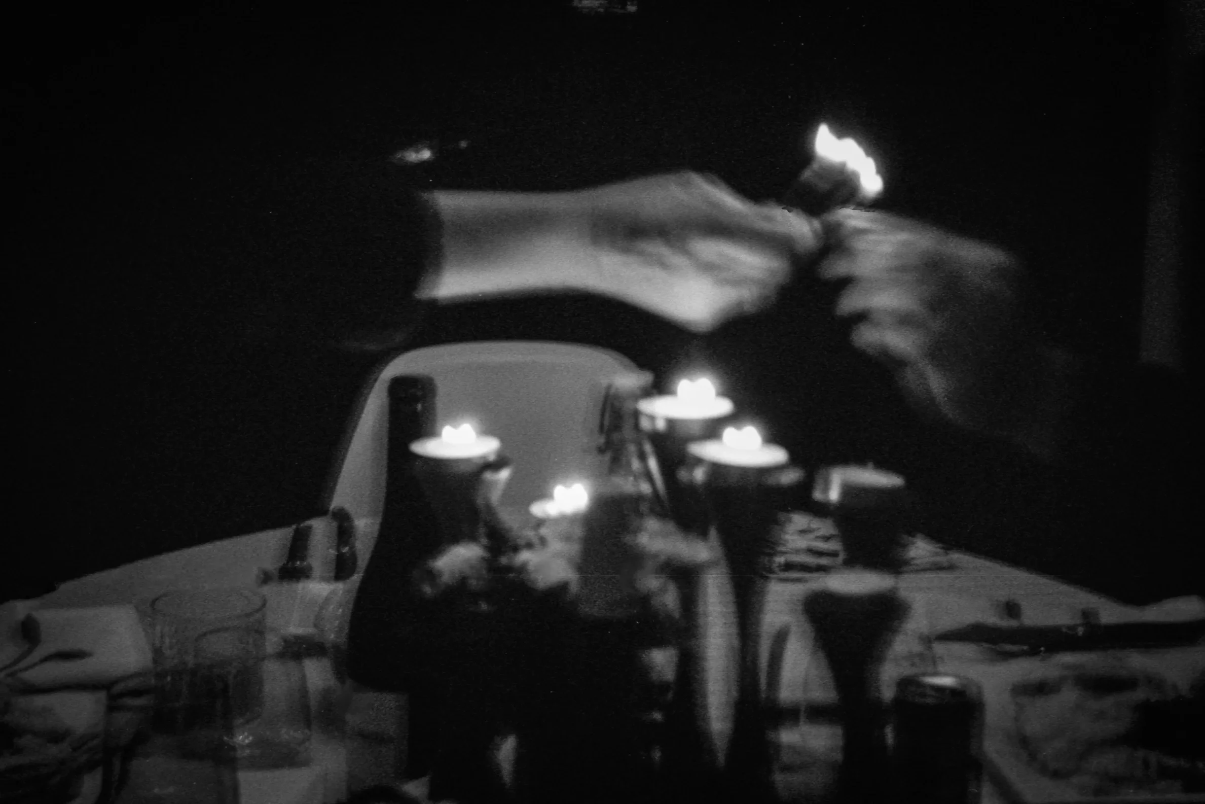 A dark room with a table decorated with lit candles, some chairs around it, and a person standing near the table.