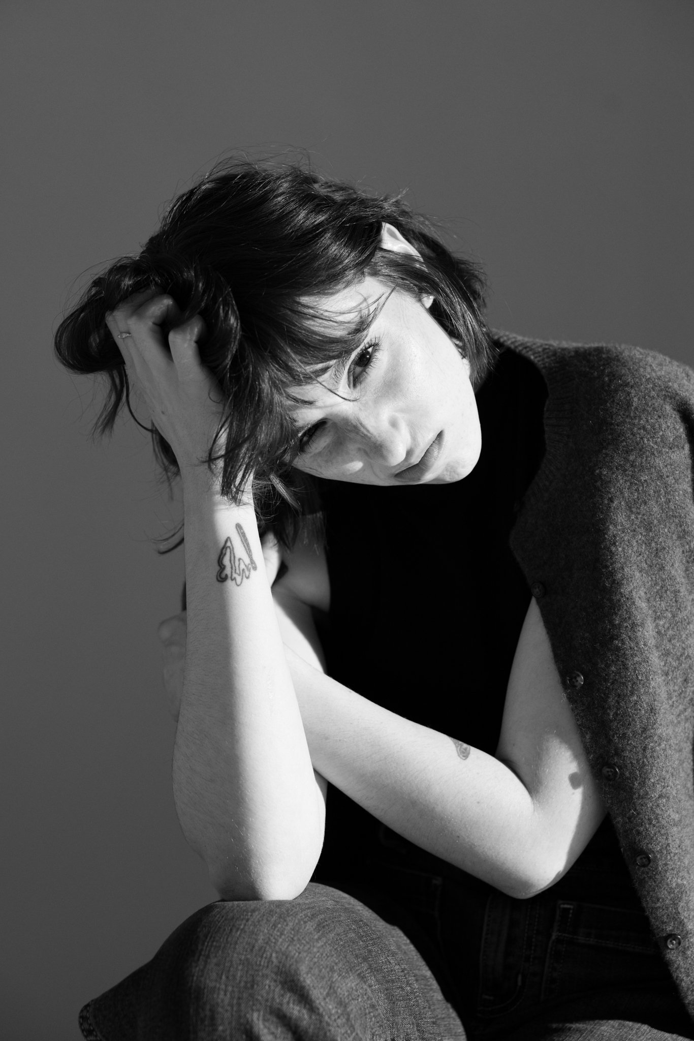 Cleo Shine is sitting with her head tilted and her hand resting on her head, looking slightly downward in a black-and-white photo.