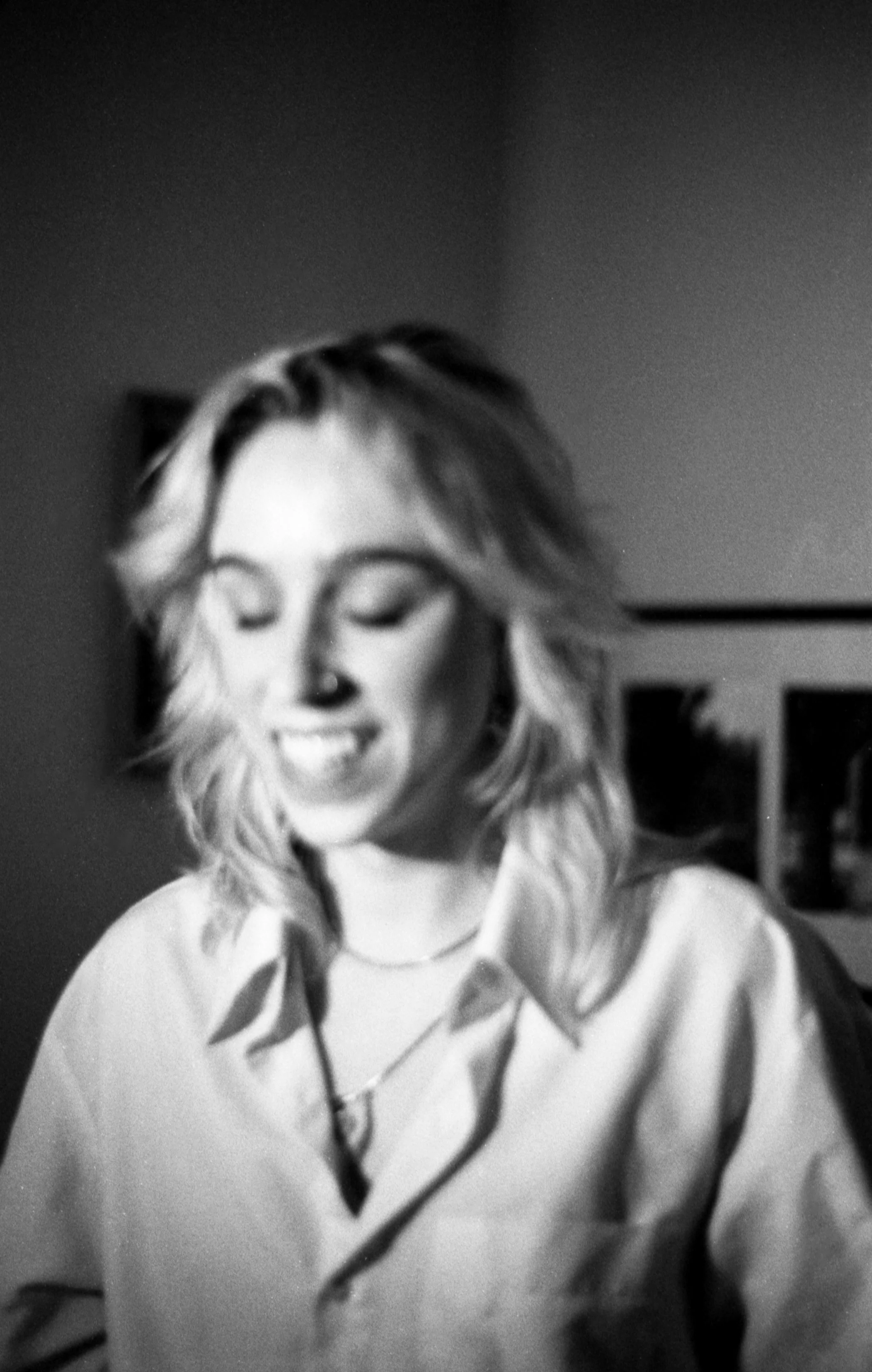 Black and white photo of Cleo Shine with shoulder-length hair, wearing a collared shirt, smiling with eyes closed.