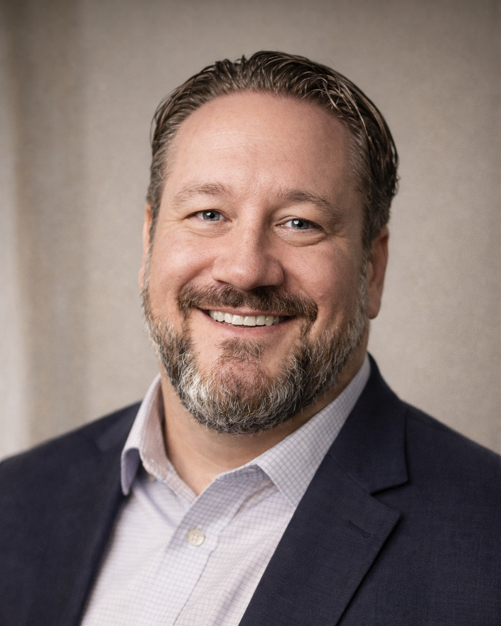 A man with a beard and short hair smiling, wearing a plaid blazer over a dark polo shirt, standing in front of a dark blue background with a logo that reads 'MJYC.tech'.