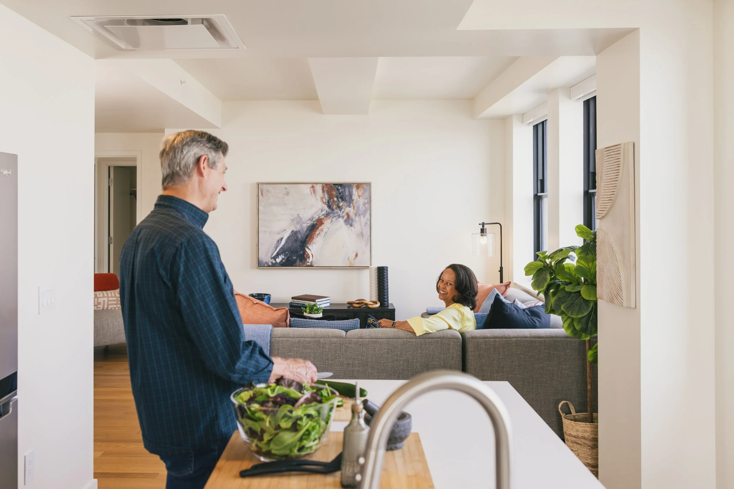 A man, standing, and a woman, sitting on the couch, talking in the living area of a unit at Book Tower.