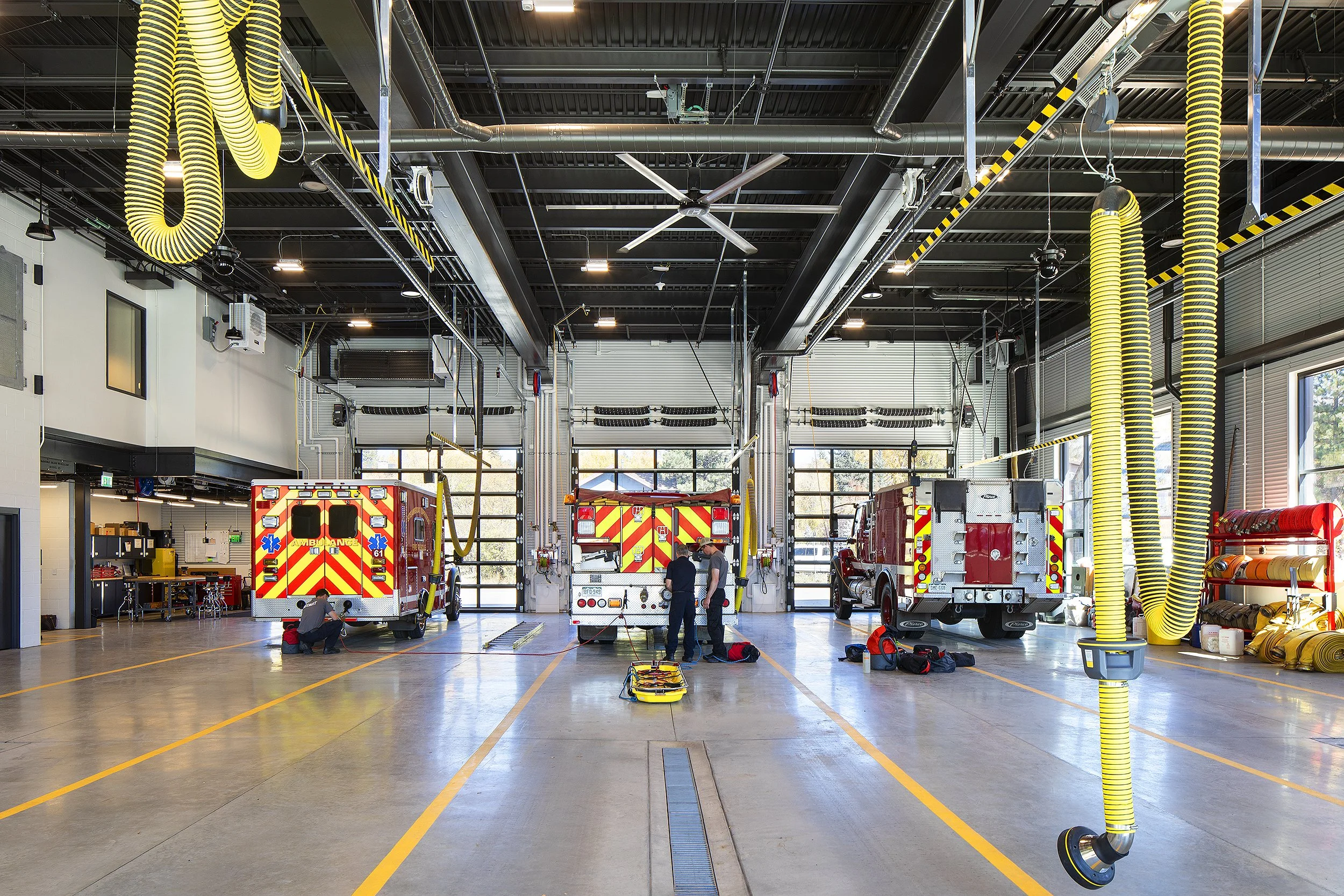 Interior of fire station bay and fire trucks yellow hoses hanging 