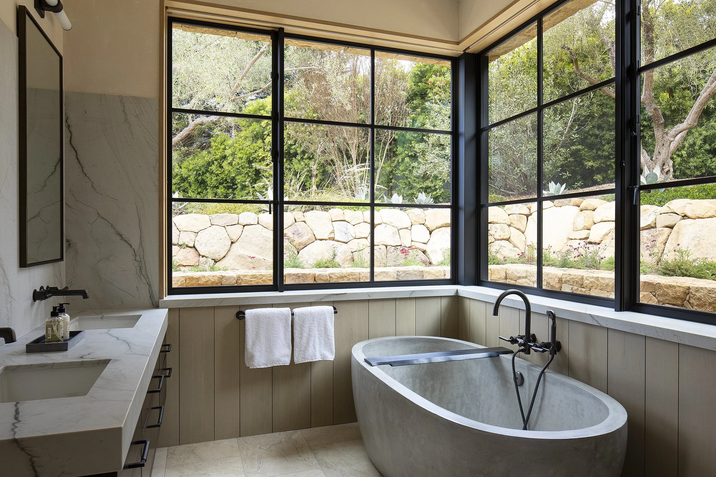 Sone tub in bathroom with view out into foliage and stone wall 