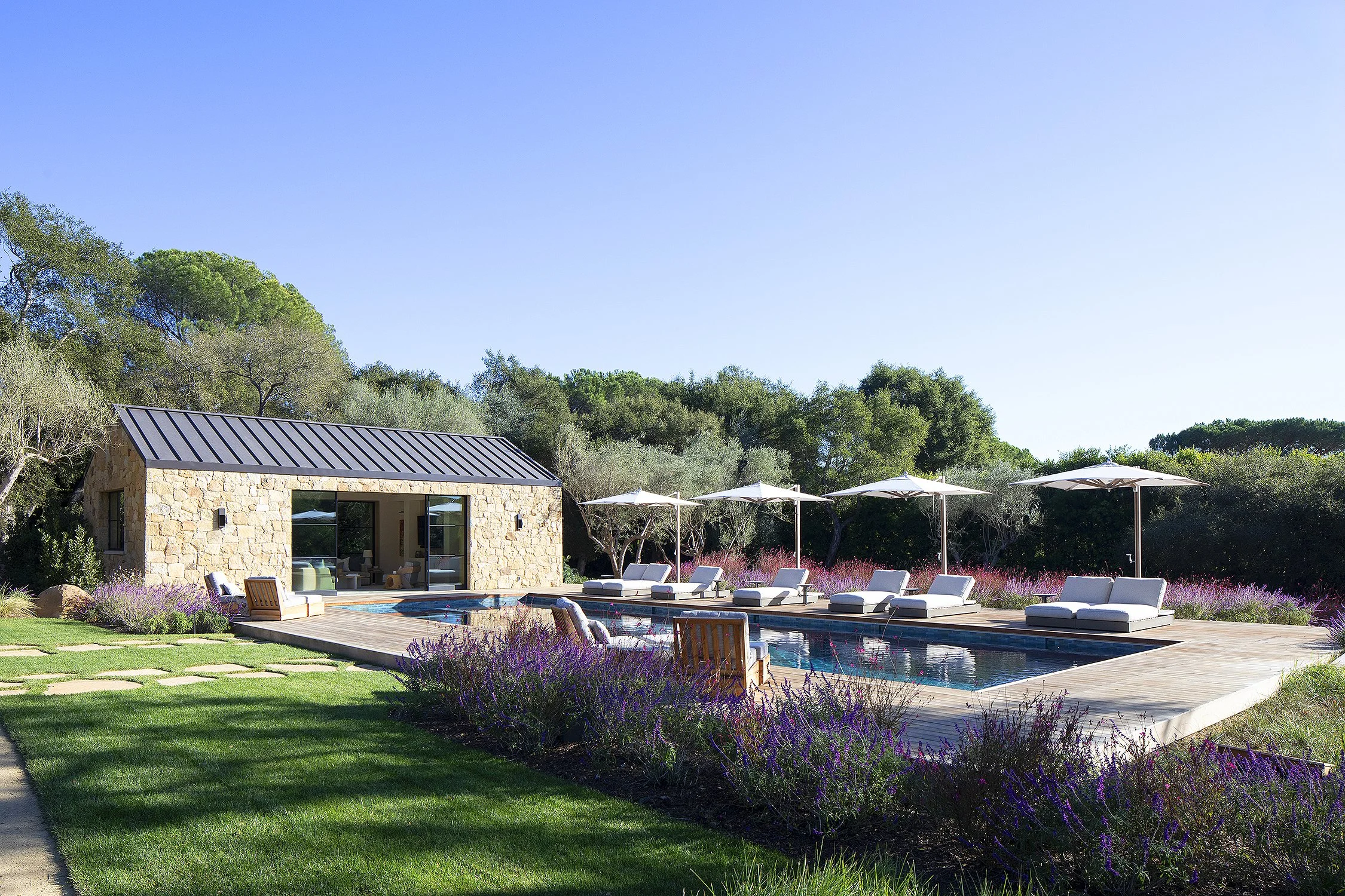 Pool setting and pool house with white umbrellas and chairs in a Montecito California home