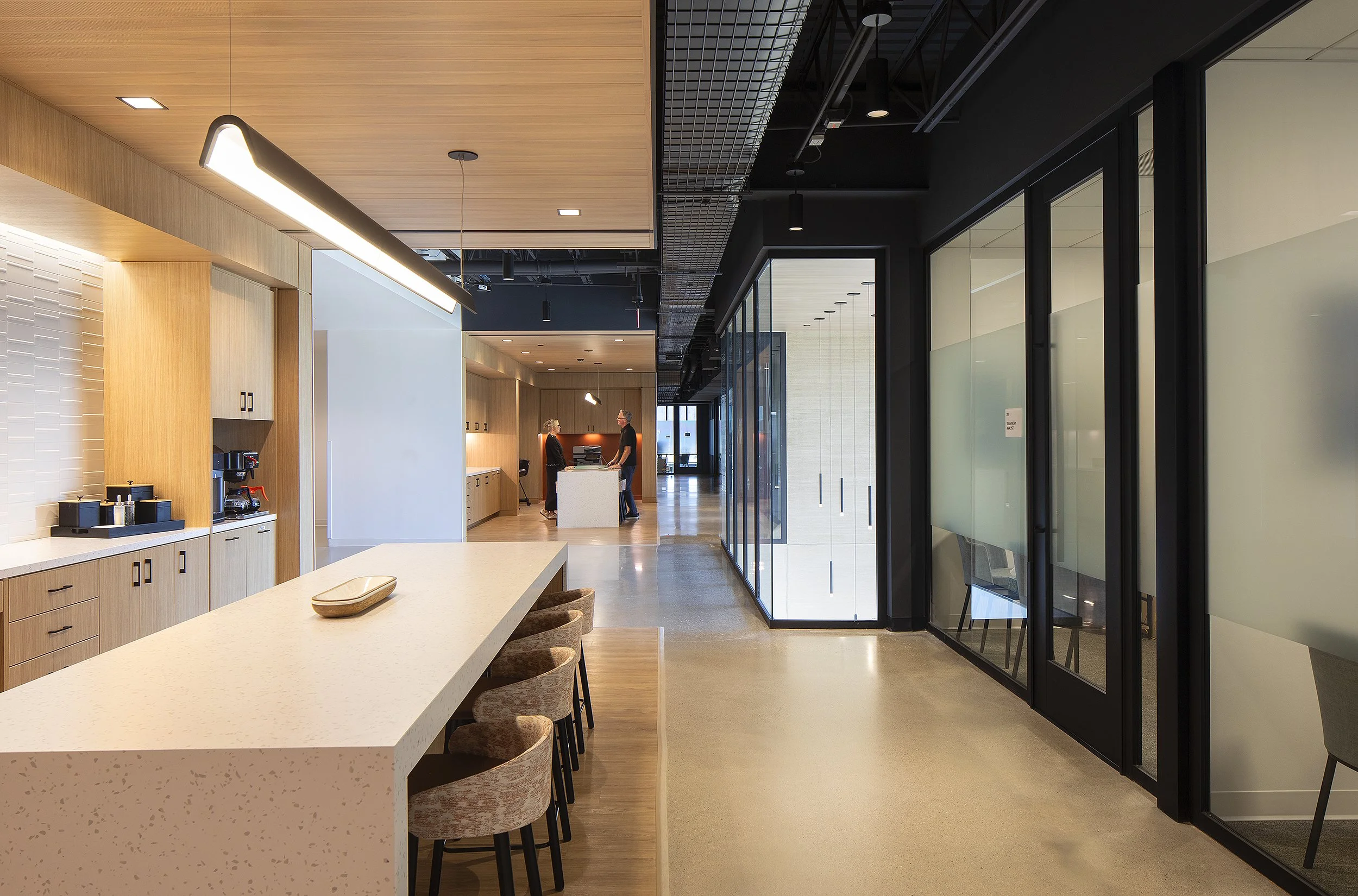 Office break room with large White Island and two people in the background conversing