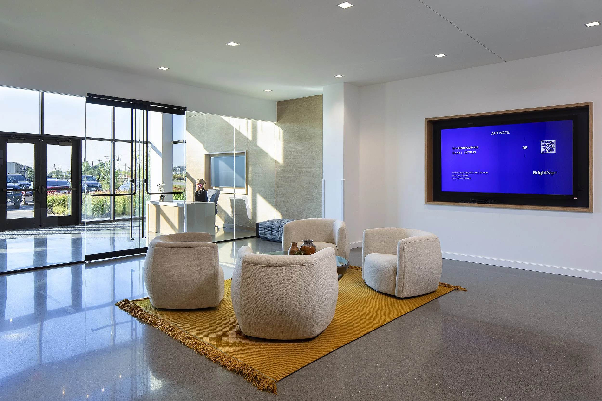 Office reception area with four white chairs and receptionist at here desk on the phone 