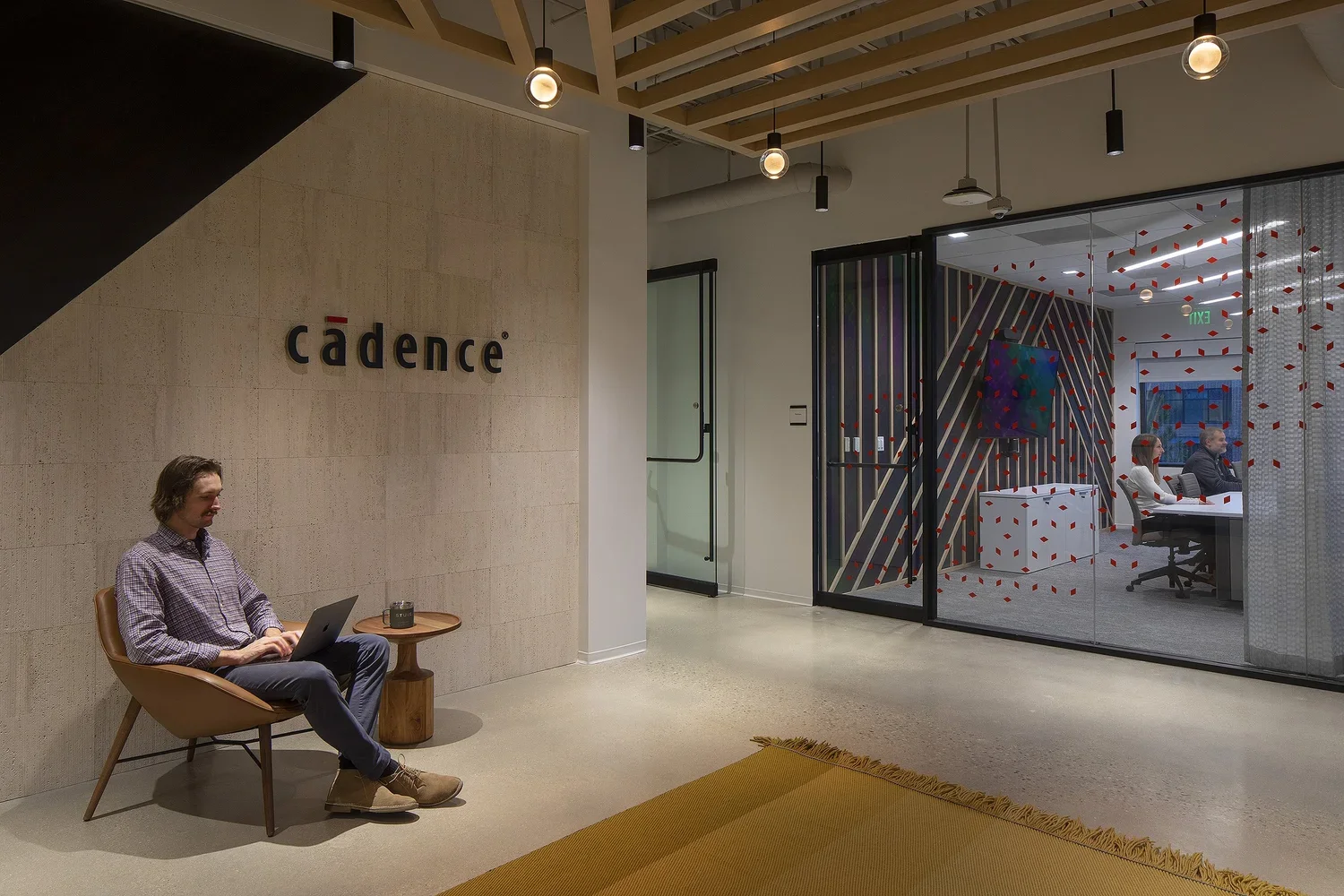 Man sitting in lobby with laptop and conference room in the background with people 